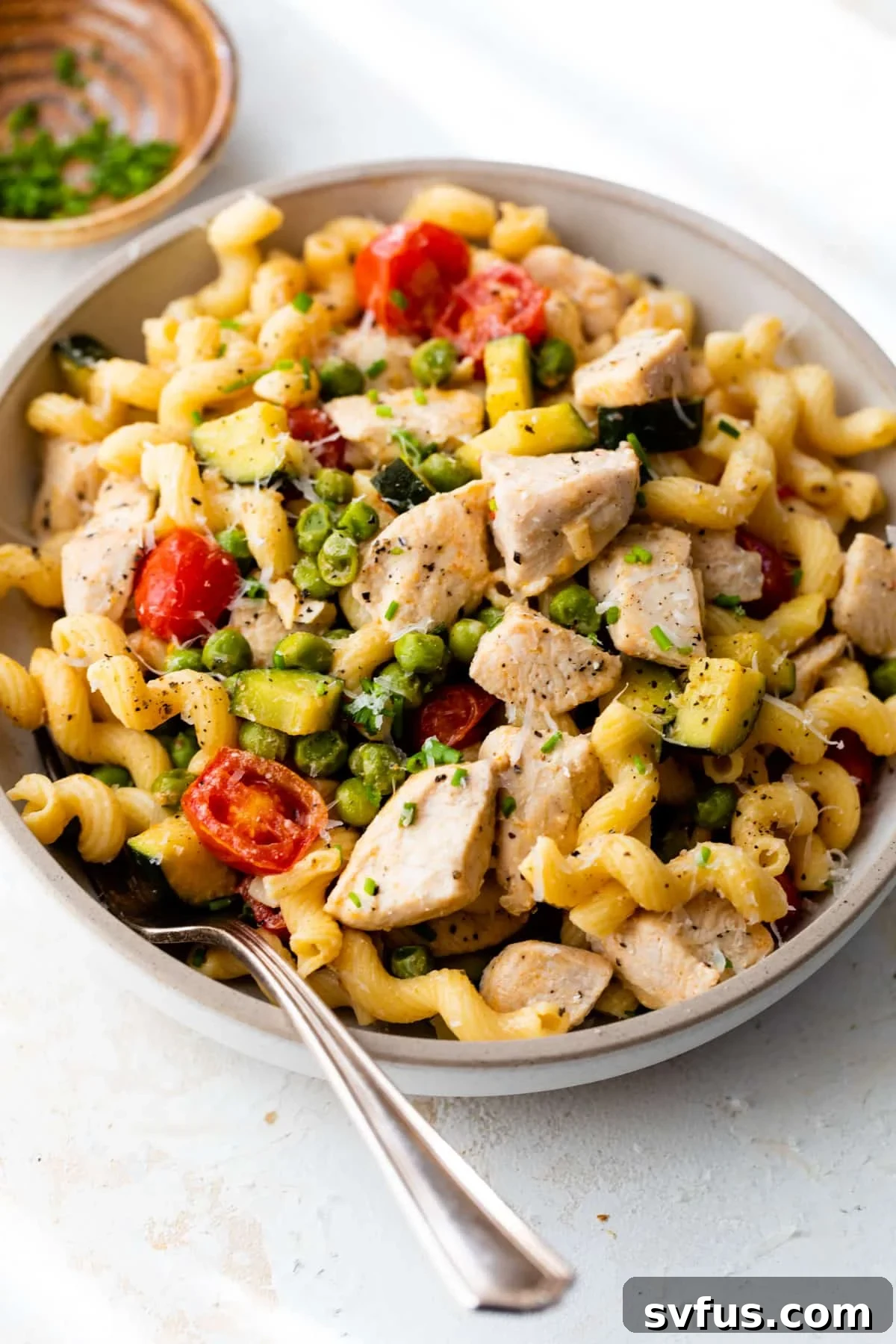 A close-up shot of creamy Chicken Pasta Primavera served in a bowl, garnished with fresh herbs, with a fork ready to dig in.