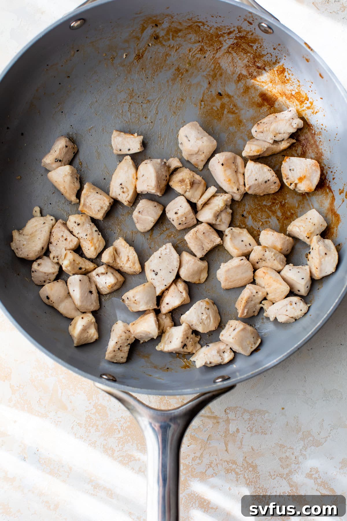 Diced chicken pieces cooking in a hot skillet, browning nicely.