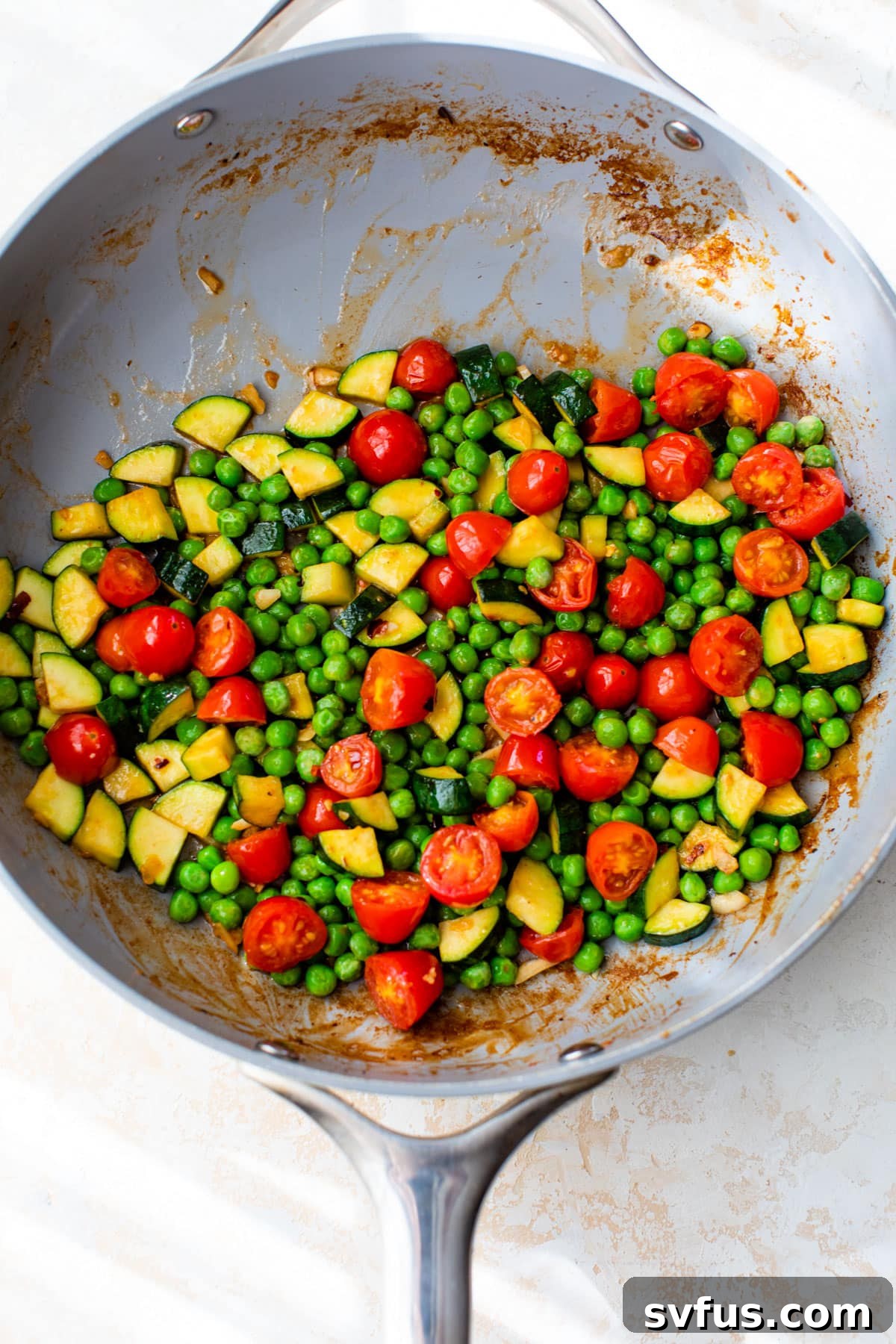 Chopped zucchini, grape tomatoes, and green peas sautéing in a skillet, looking vibrant and tender-crisp.
