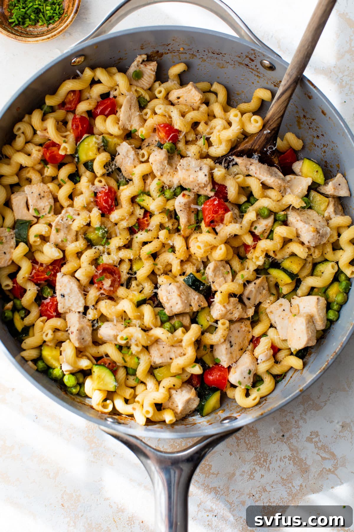 Close-up of finished Chicken Pasta Primavera in a bowl, with a fork, showing pasta, chicken, and vegetables coated in a creamy sauce, garnished with herbs and parmesan.
