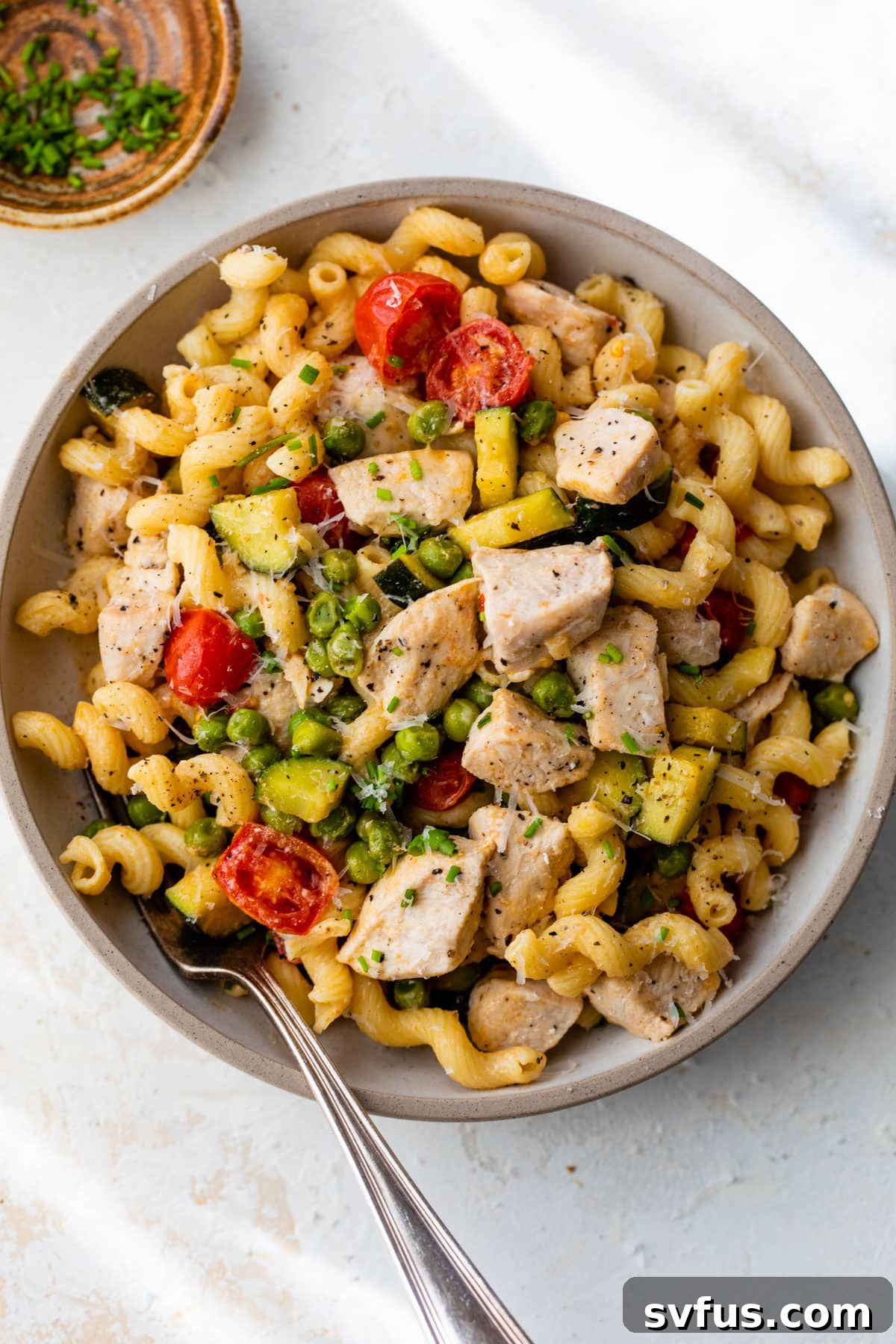 A serving of chicken pasta primavera in a bowl with a fork, ready to be eaten, showcasing its creamy sauce and fresh ingredients.