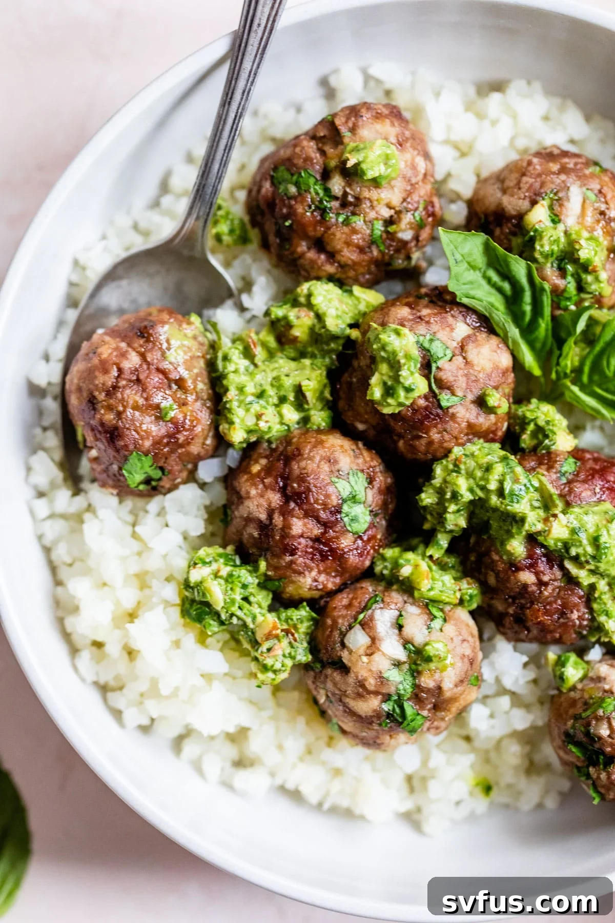 cauliflower rice in a bowl topped with meatballs and pesto