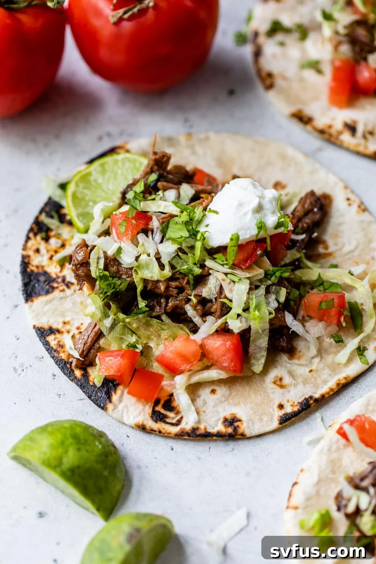 crockpot beef tacos on a tortilla with lettuce, tomatoes, and a dollop of sour cream