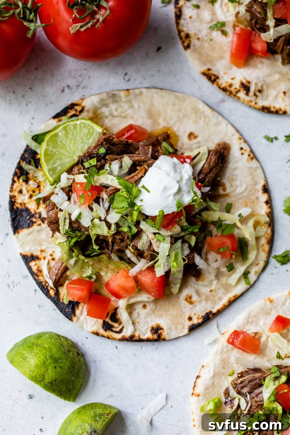crockpot beef tacos on a tortilla with lettuce, tomatoes, and a dollop of sour cream