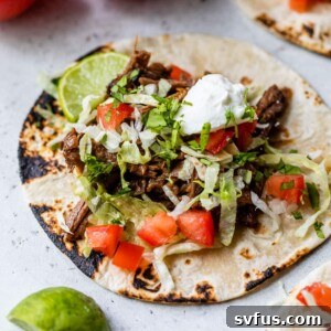 crockpot beef tacos on a tortilla with lettuce, tomatoes, and a dollop of sour cream