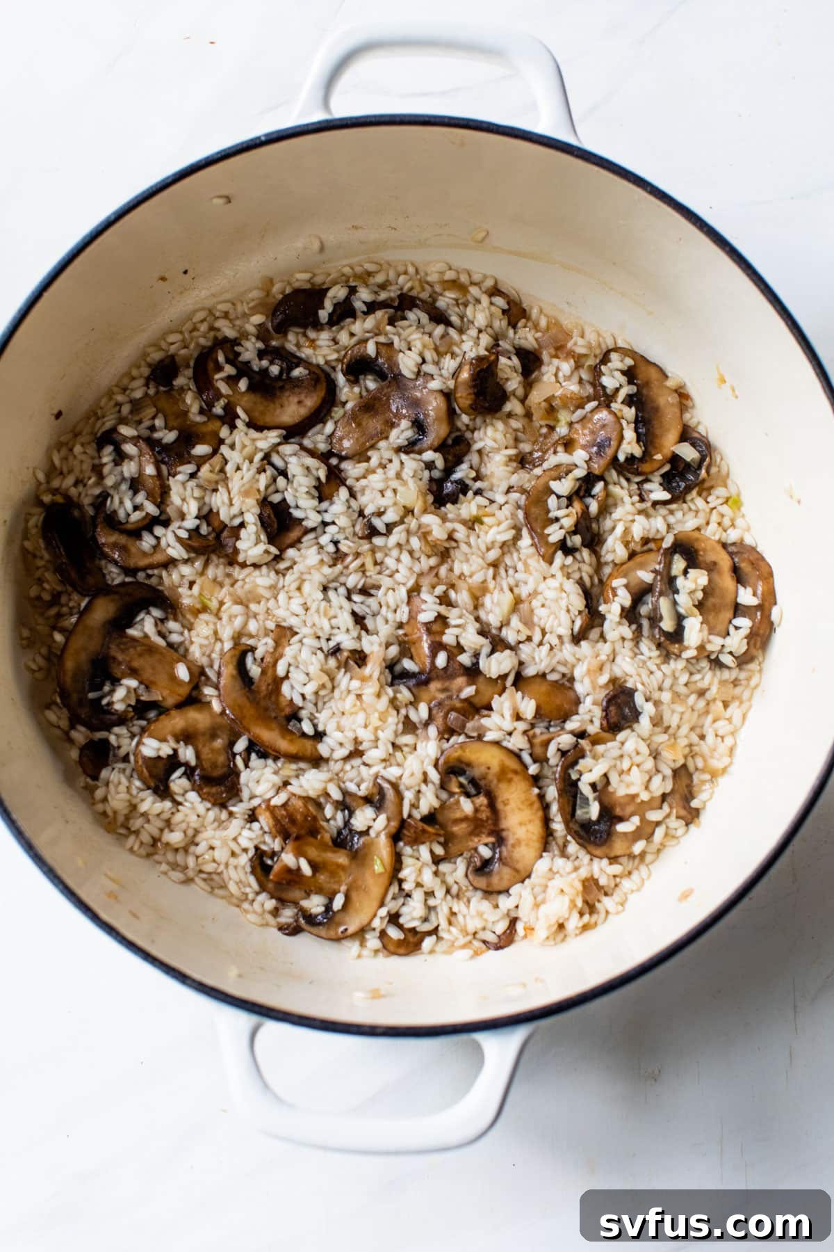 Arborio rice added to a Dutch oven with cooked mushrooms and aromatics, preparing for liquid addition