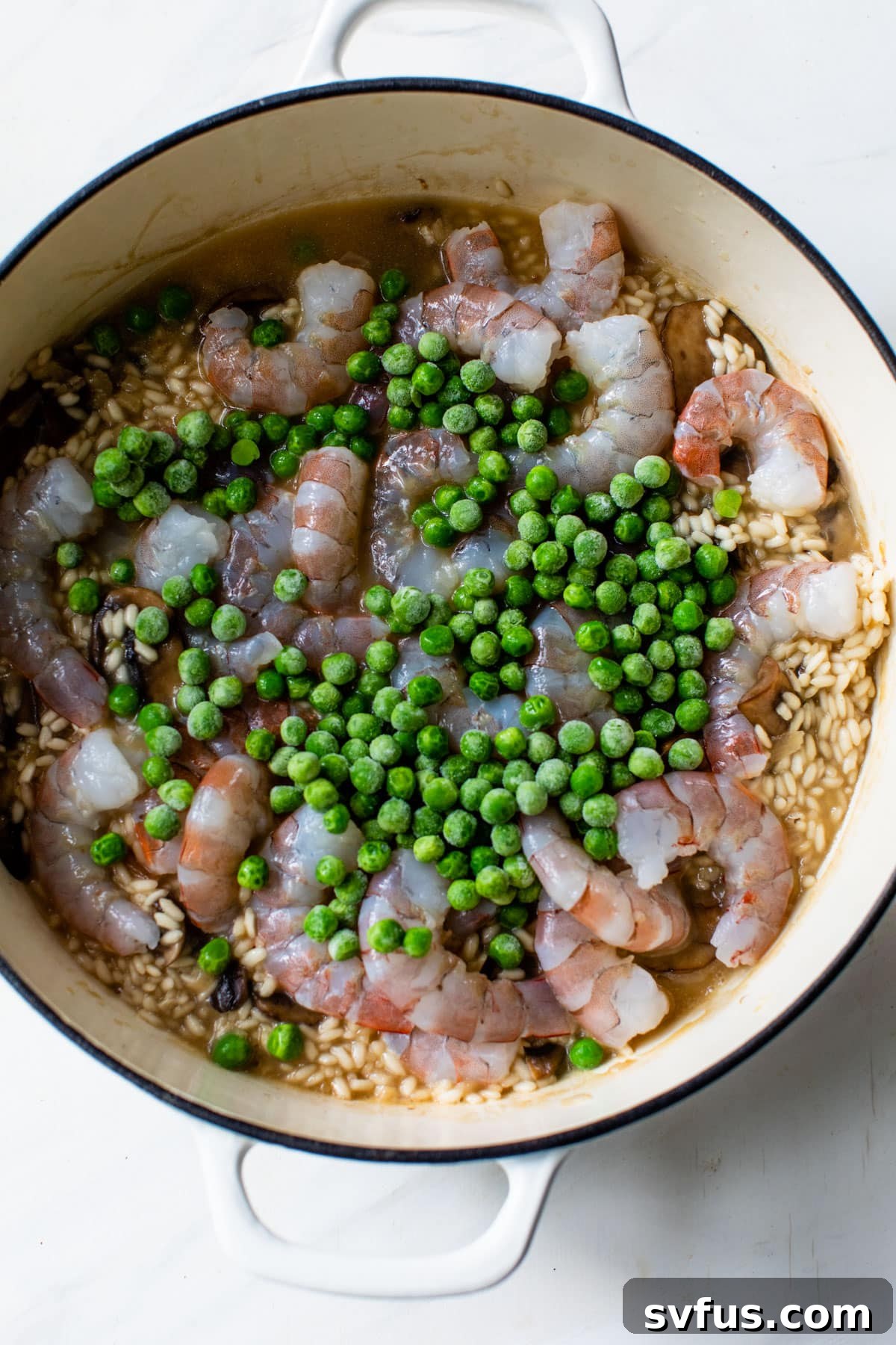 Shrimp and frozen peas added on top of creamy risotto in a Dutch oven, simmering
