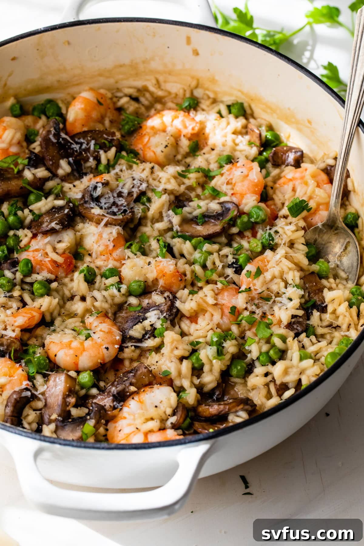 Side view of creamy shrimp risotto in a Dutch oven with a spoon, garnished with fresh parsley