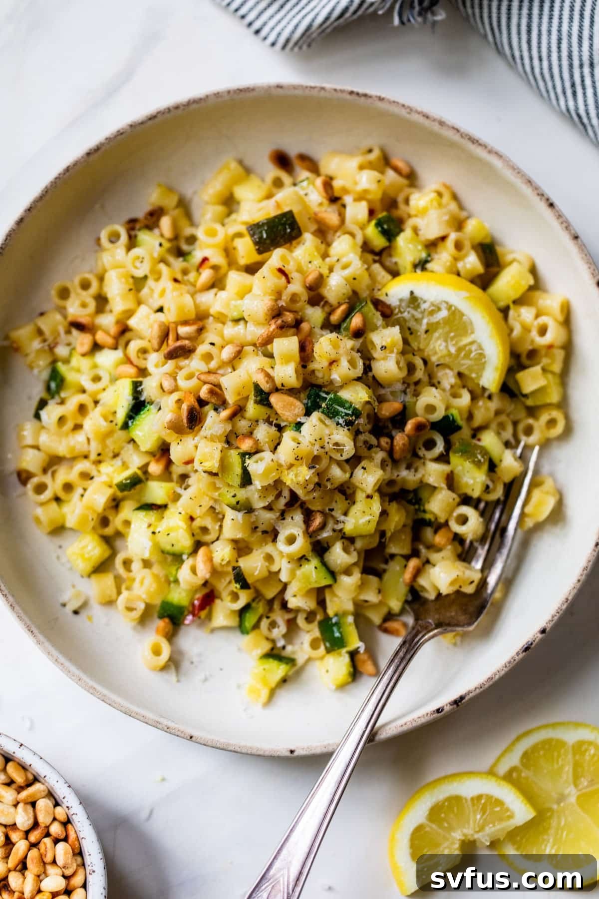 lemon zucchini pasta on a plate with a lemon slice and a fork