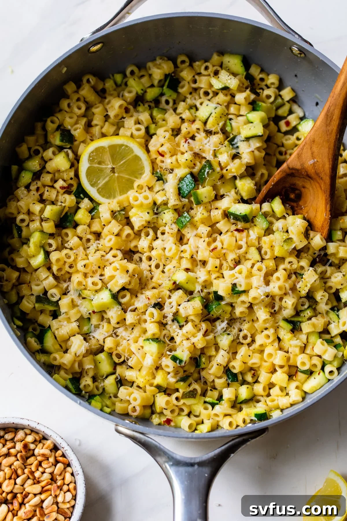 lemon zucchini pasta in a skillet with a lemon and wooden spoon