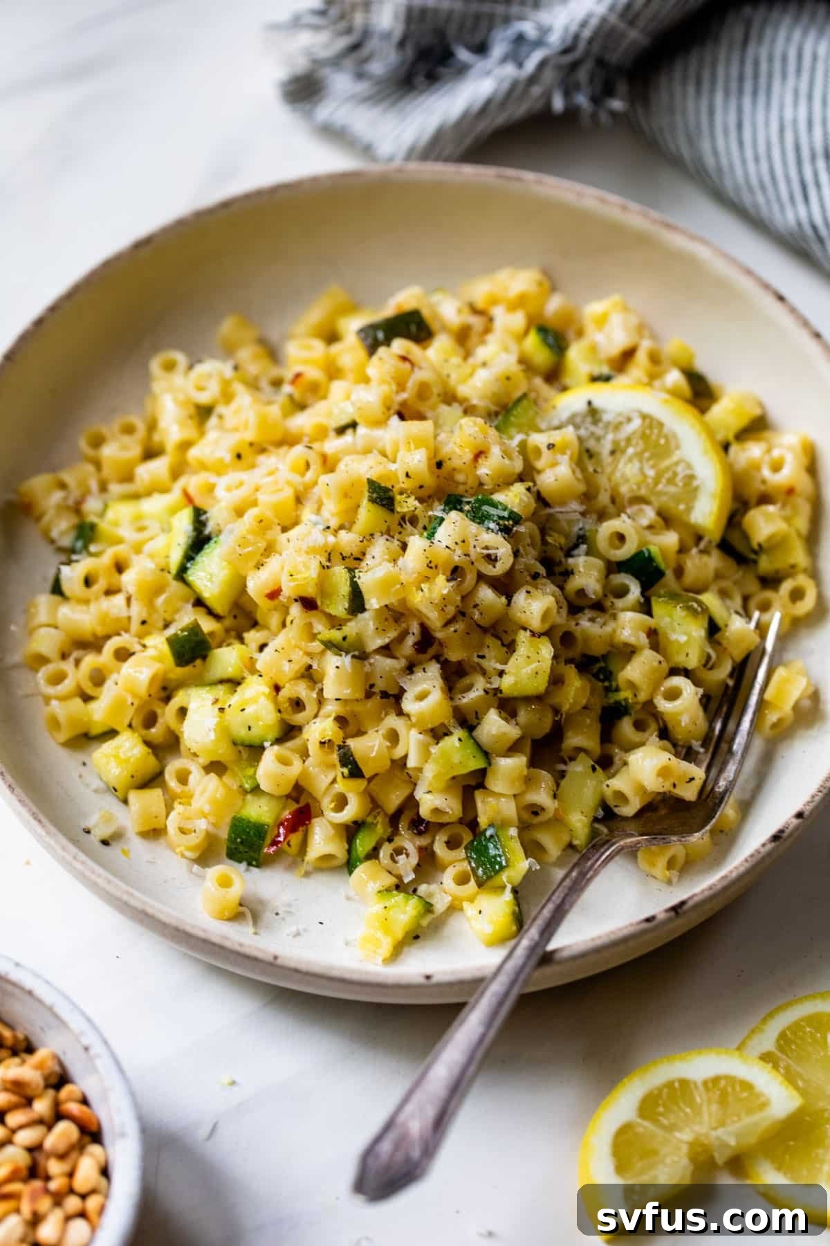 lemon zucchini pasta on a plate with a lemon slice and a fork