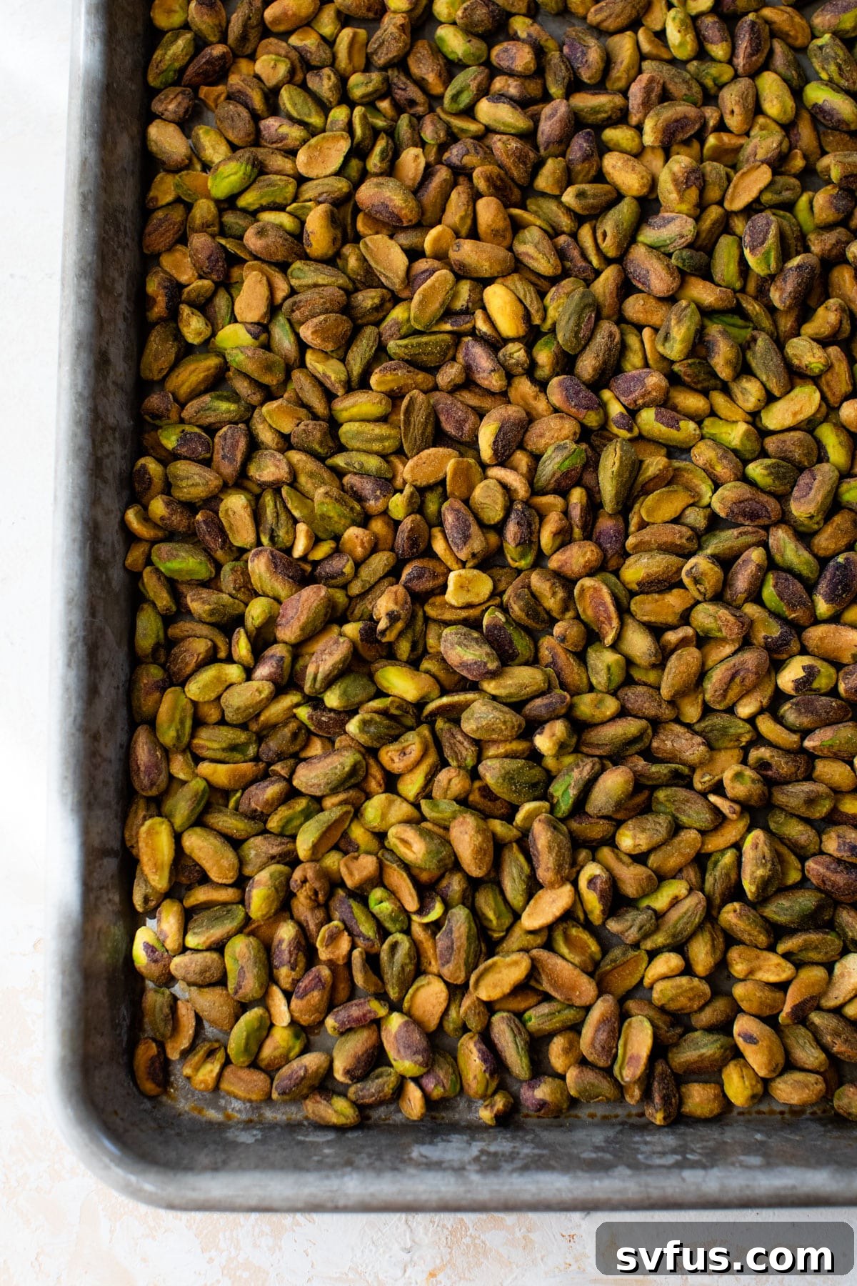 Raw shelled pistachios spread evenly on a parchment-lined baking sheet, ready for toasting.