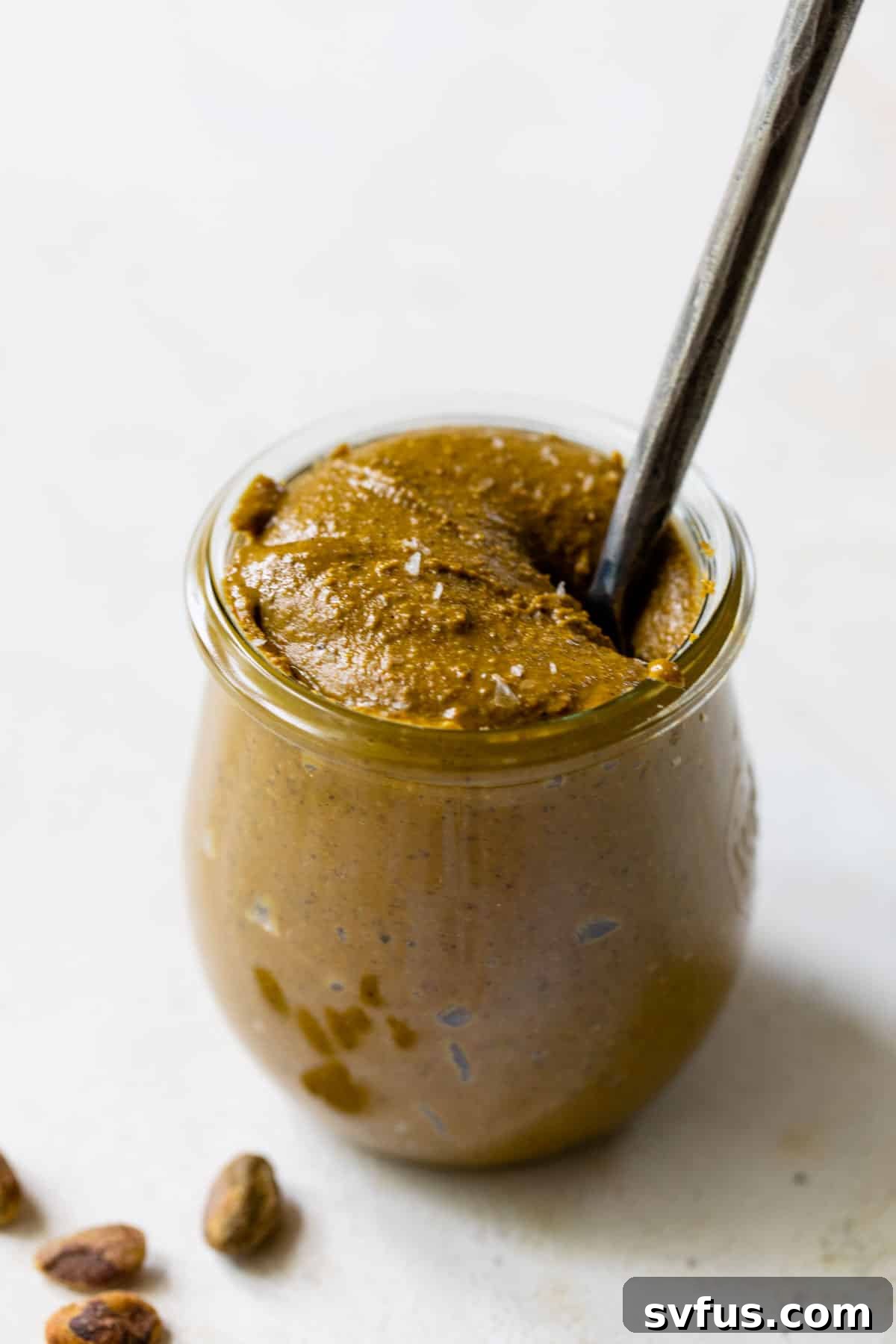 A glass jar filled with vibrant green homemade pistachio butter, with a small knife dipped inside, ready to be enjoyed.