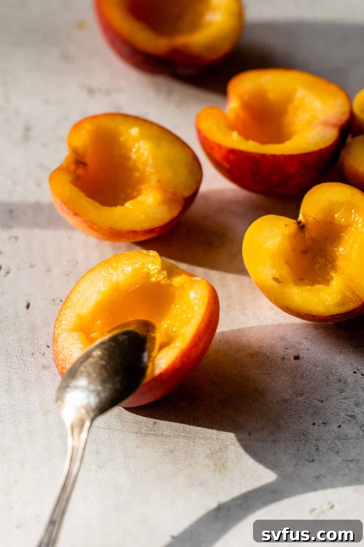 Pits removed from peach halves with a spoon, showing the preparation step for baked peaches.