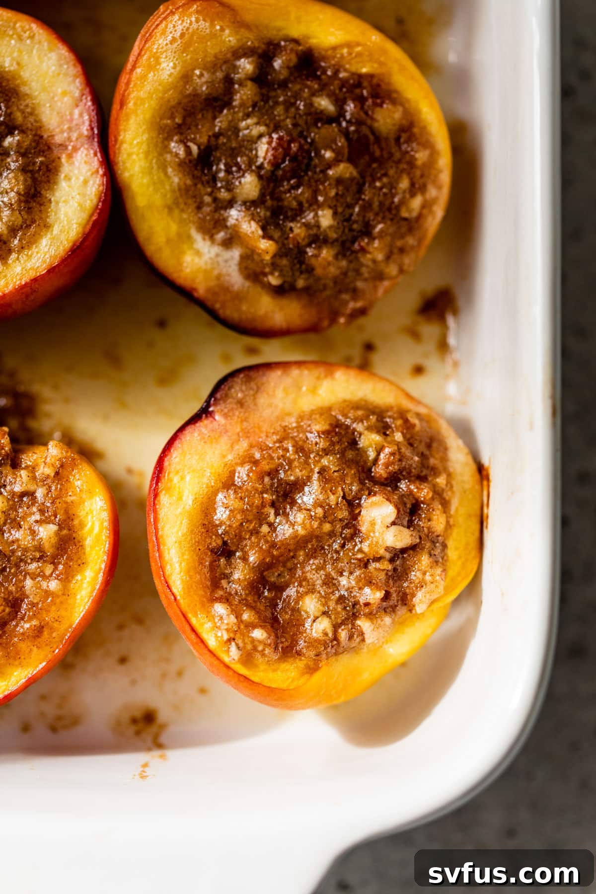 Close-up of baked peaches with pecan filling in a baking dish, fresh from the oven.
