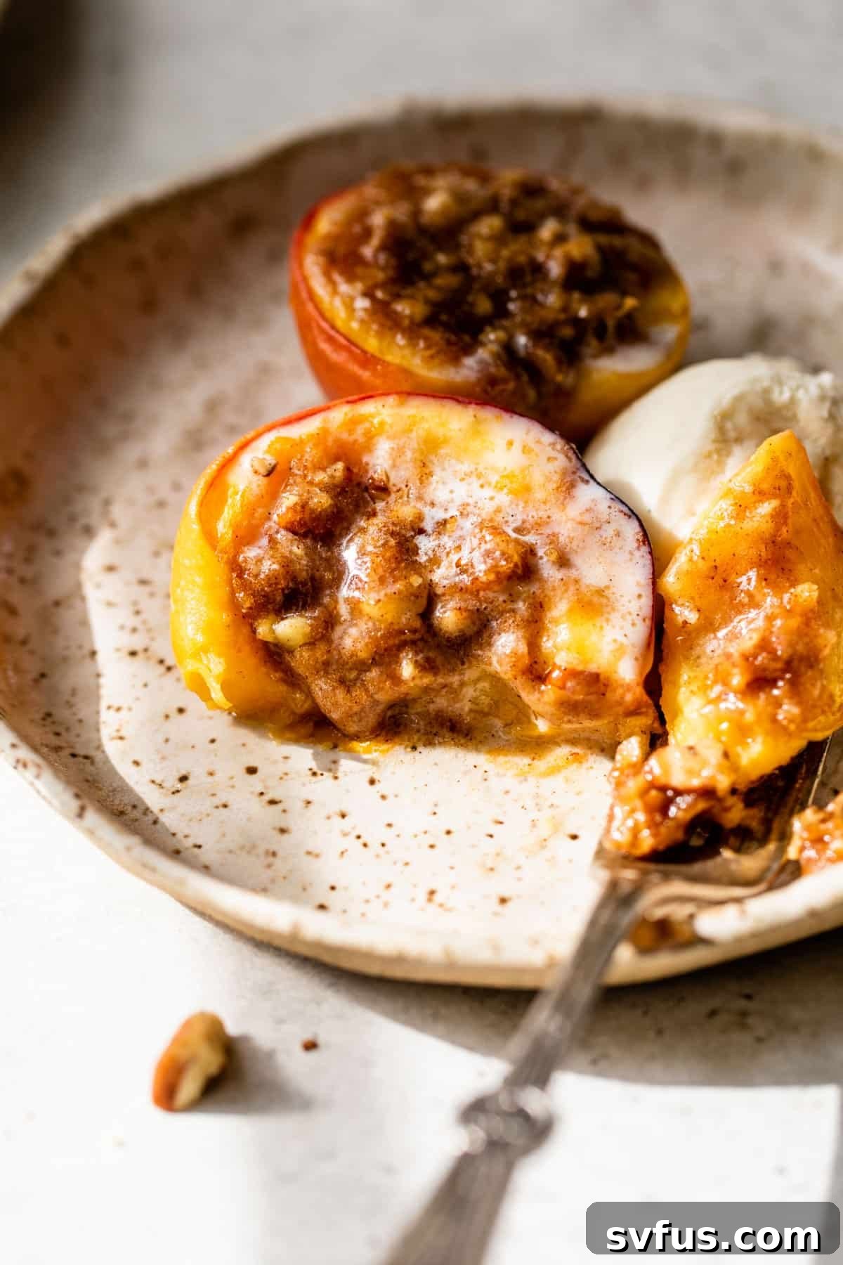 A perfectly baked peach on a white plate with a fork and a melting scoop of vanilla ice cream, highlighting the warm dessert.
