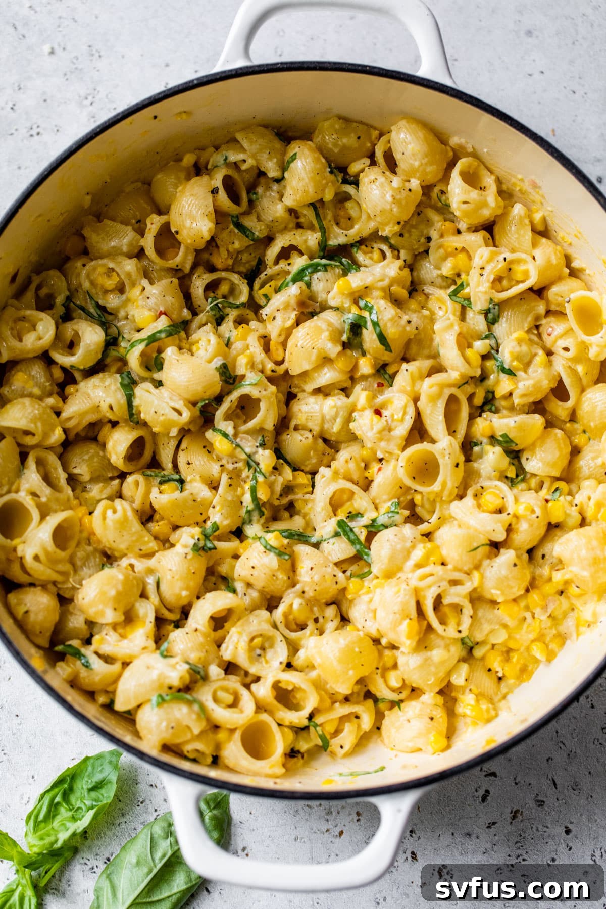 Creamy corn pasta perfectly mixed in a Dutch oven, topped with vibrant chopped basil.