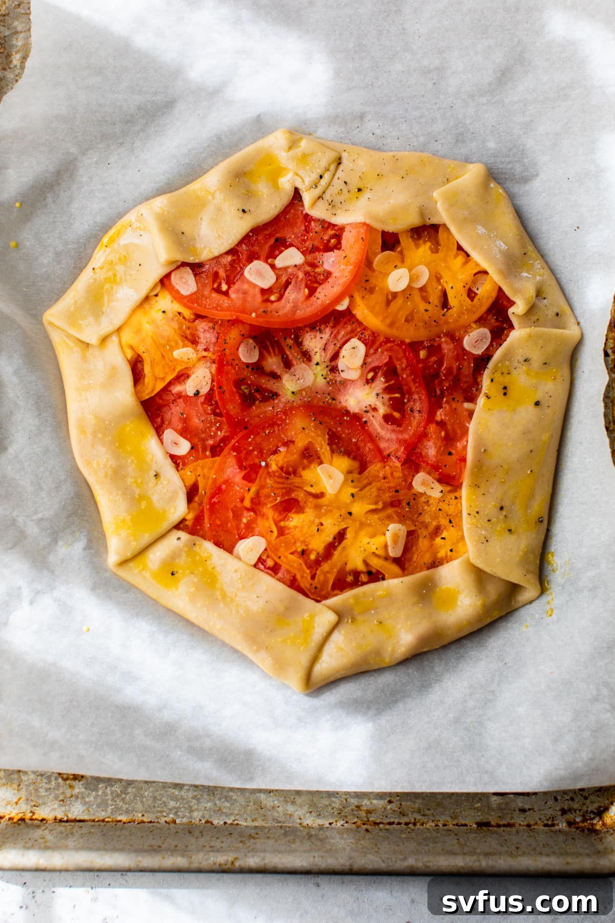 Pie dough edges folded inward over the layered tomatoes and garlic slices, creating the rustic galette shape, with the egg wash applied.
