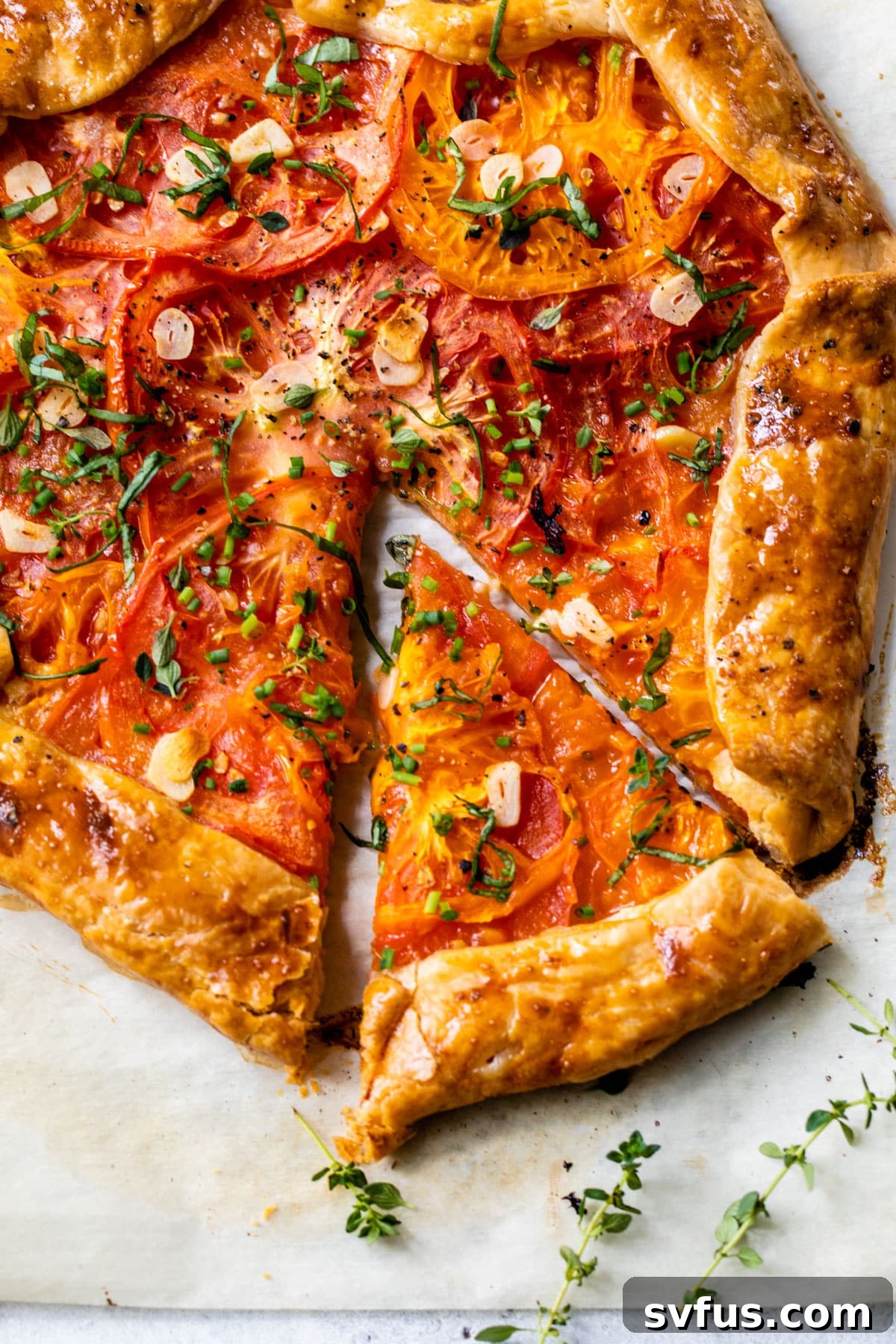 A freshly baked tomato galette, golden brown and crisp, topped with fresh thyme and chives, with a single slice removed.
