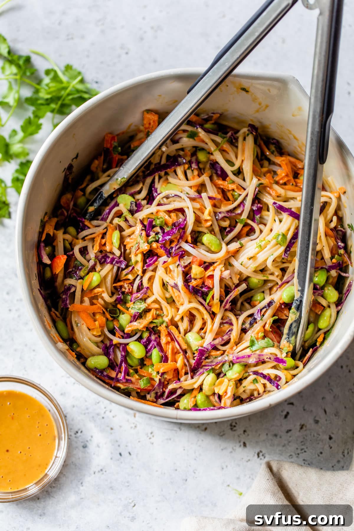 Thai noodle salad in a large bowl, tossed together with tongs, showcasing the vibrant colors and creamy sauce.