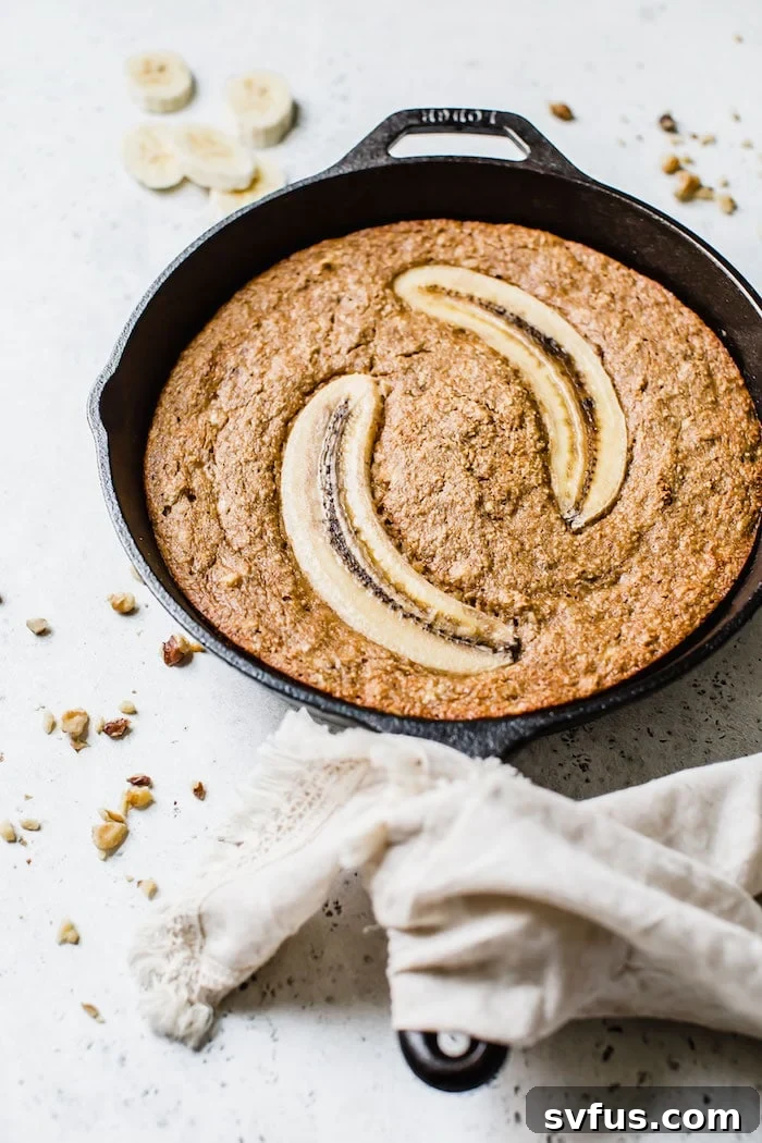 Overhead shot of Paleo Skillet Banana Bread in a cast iron skillet, garnished with banana slices and walnuts.