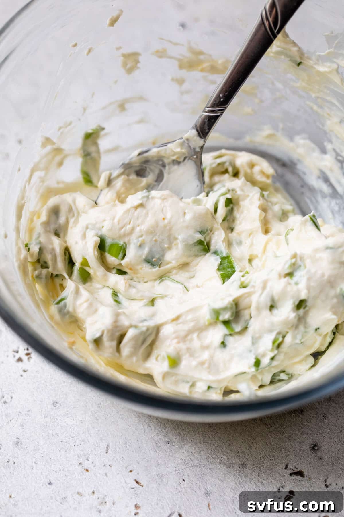scallion cream cheese in a glass bowl with a spoon, ready to be spread