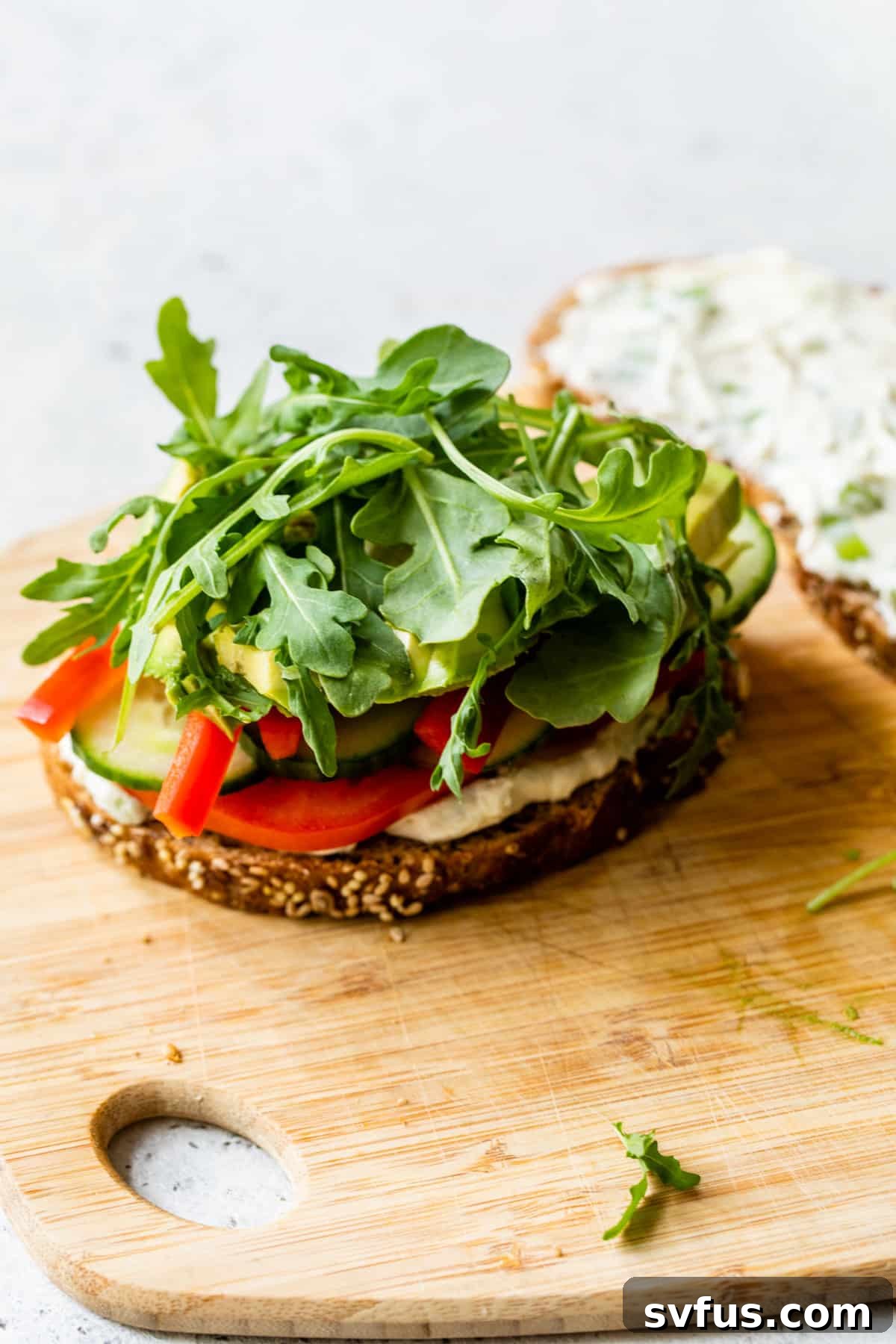 arugula and veggies stacked on top of a piece of bread with cream cheese on a cutting board