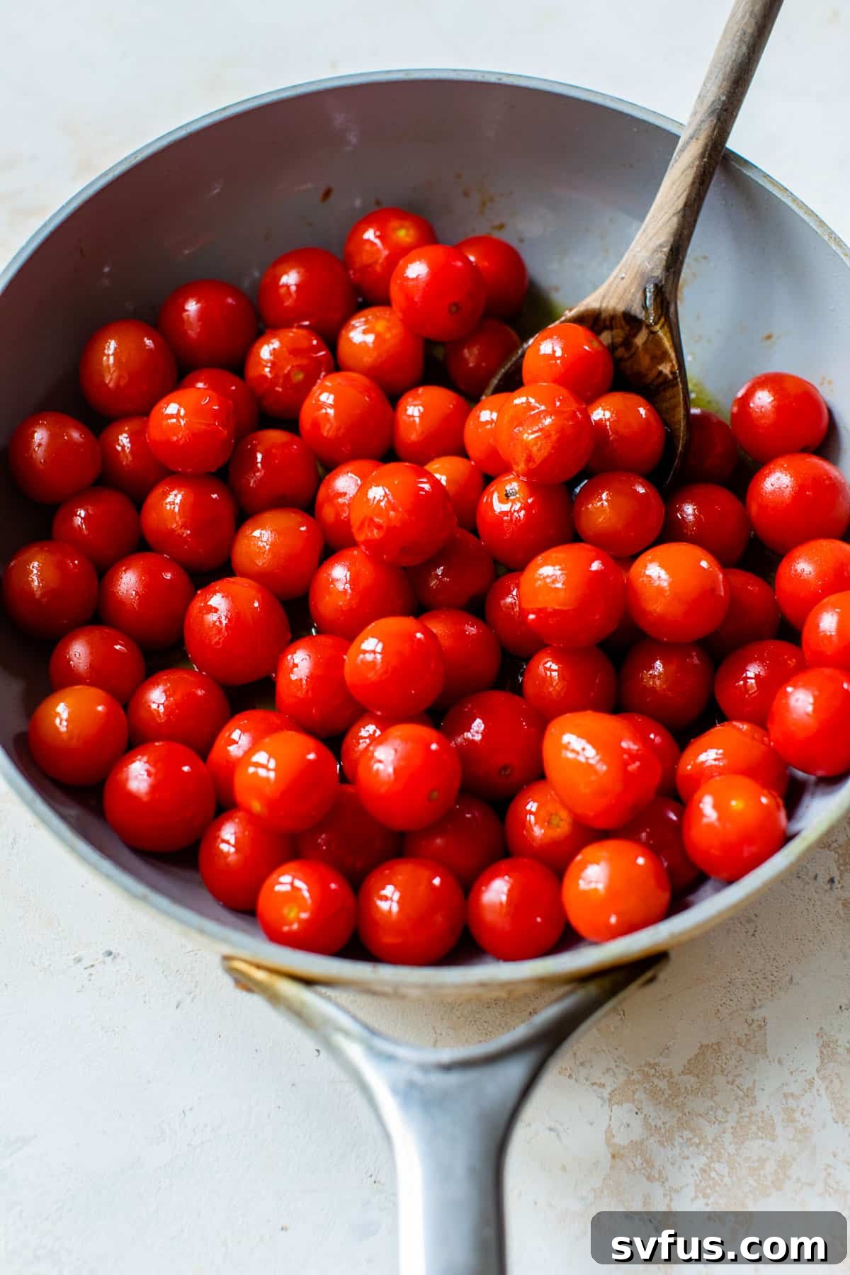 Cherry tomatoes gently sautéing in olive oil within a large skillet, ready to burst and release their juices