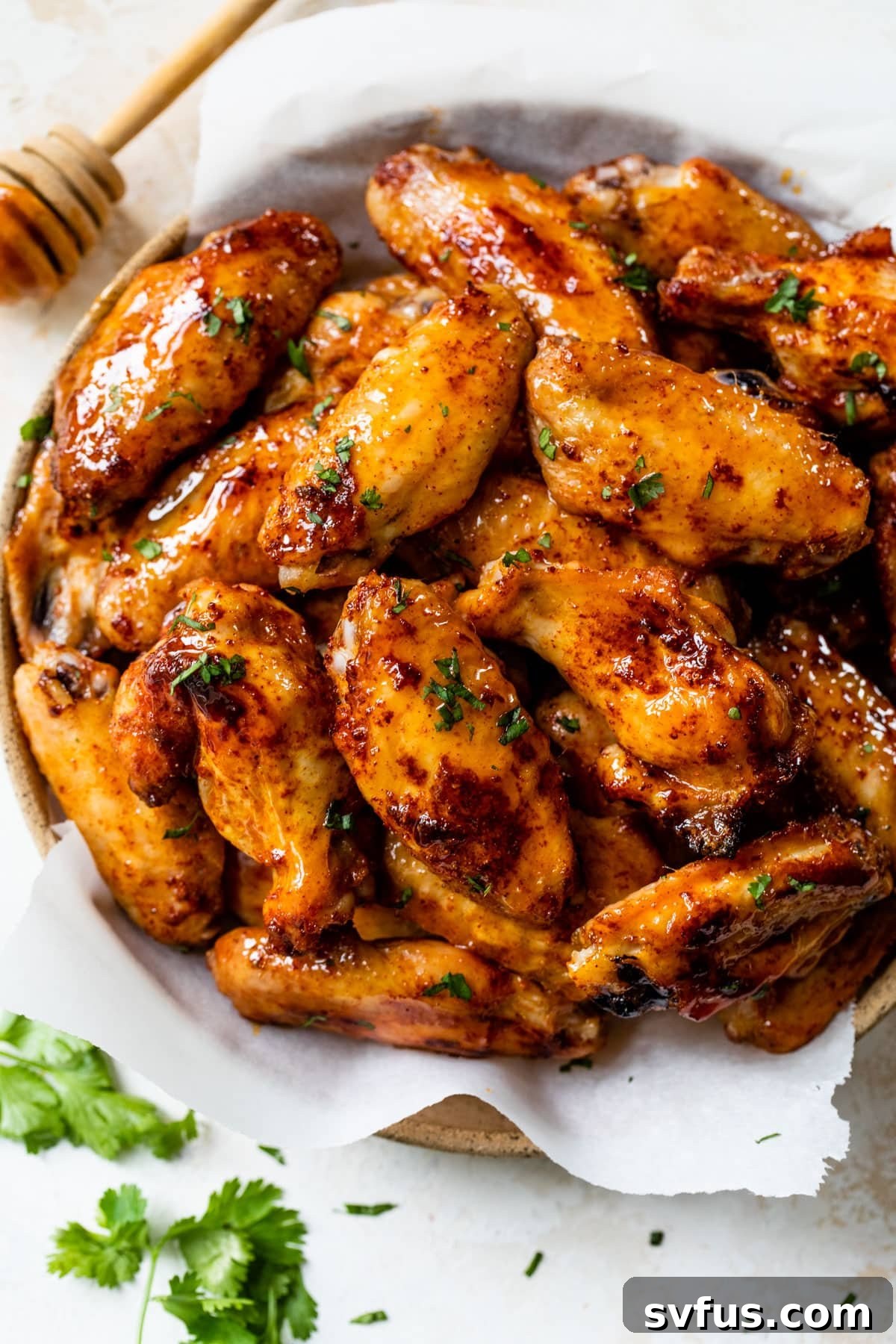 Hot honey chicken wings stacked enticingly on a rustic plate, garnished with fresh cilantro.