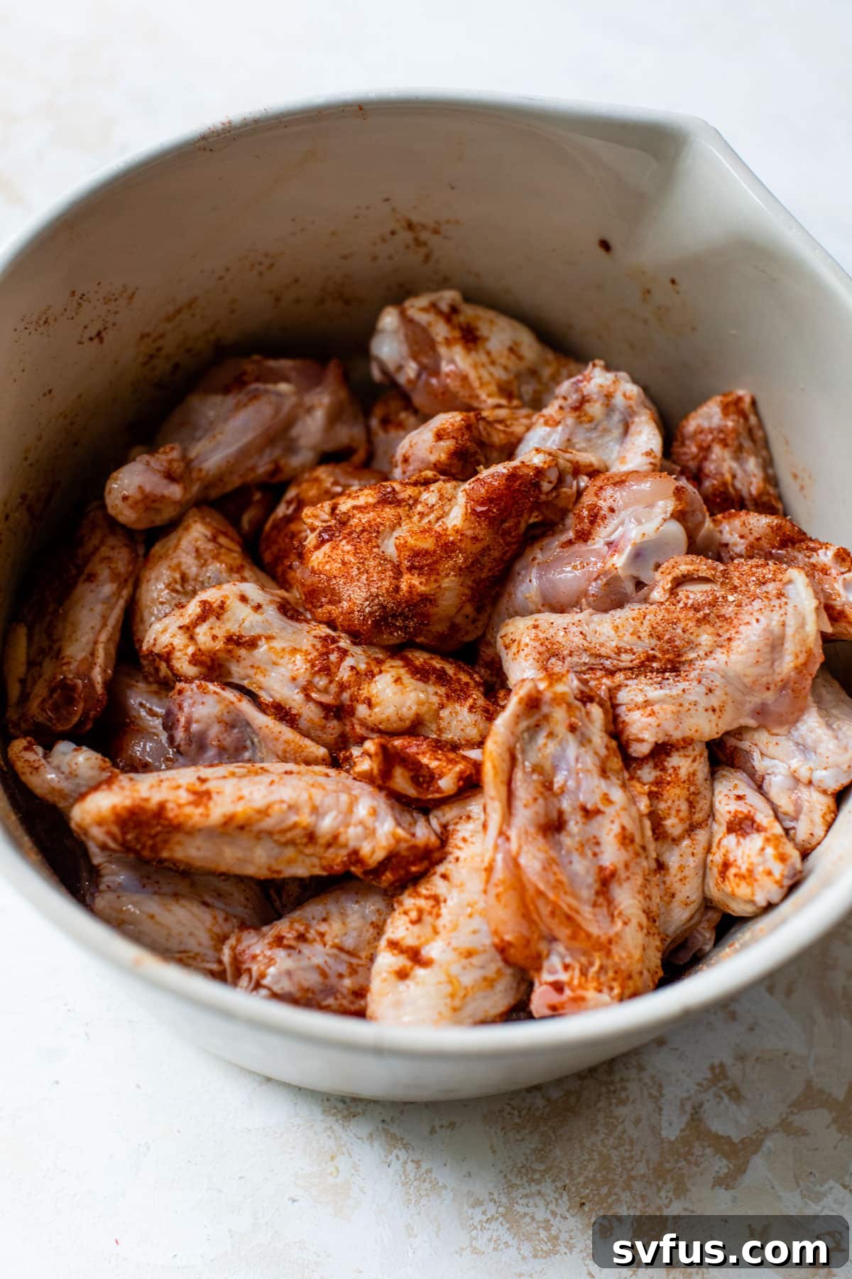 Raw chicken wings seasoned with a dry rub in a large bowl, ready for baking.