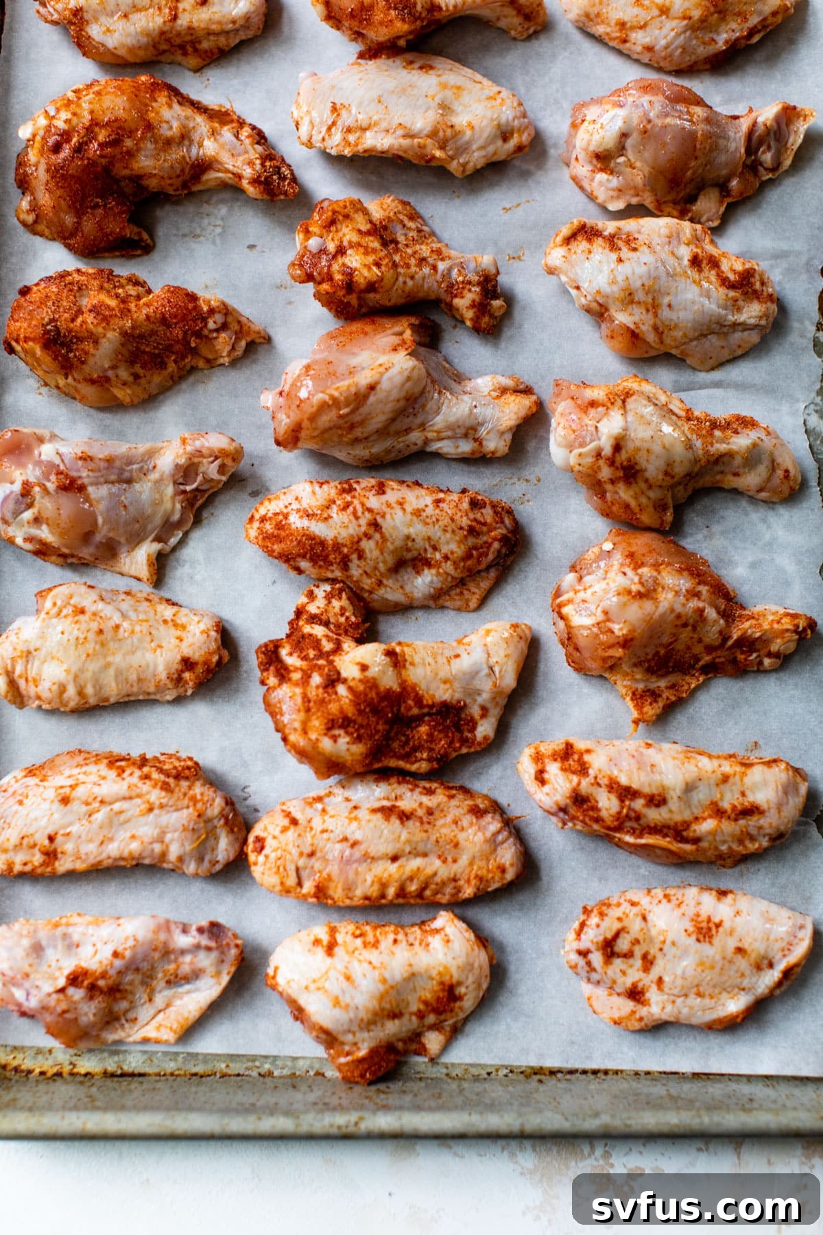 Seasoned chicken wings arranged in a single layer on a parchment-lined baking sheet, ready for the oven.