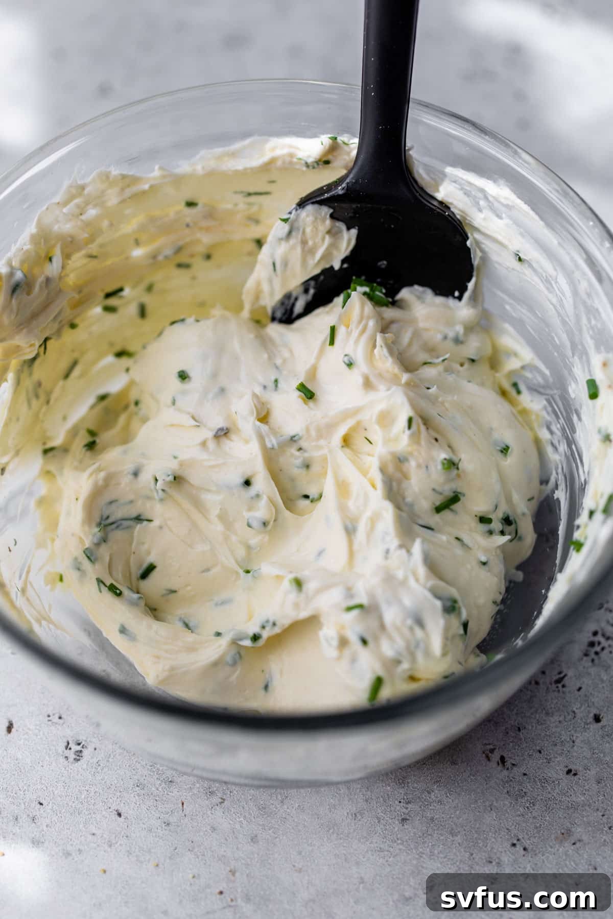 herb and garlic cream cheese mixed together in a glass bowl with a spatula