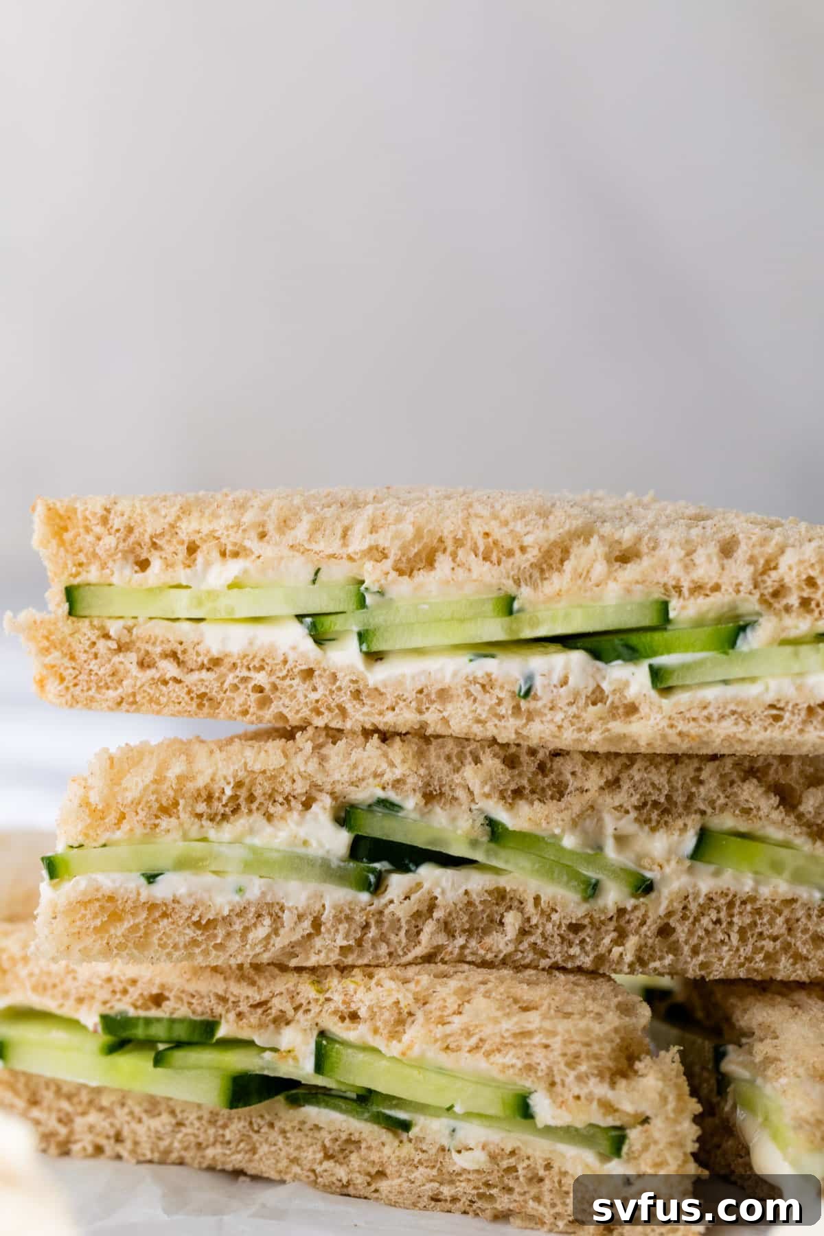 close-up of a side view of cucumber and cream cheese sandwiches stacked on top of each other