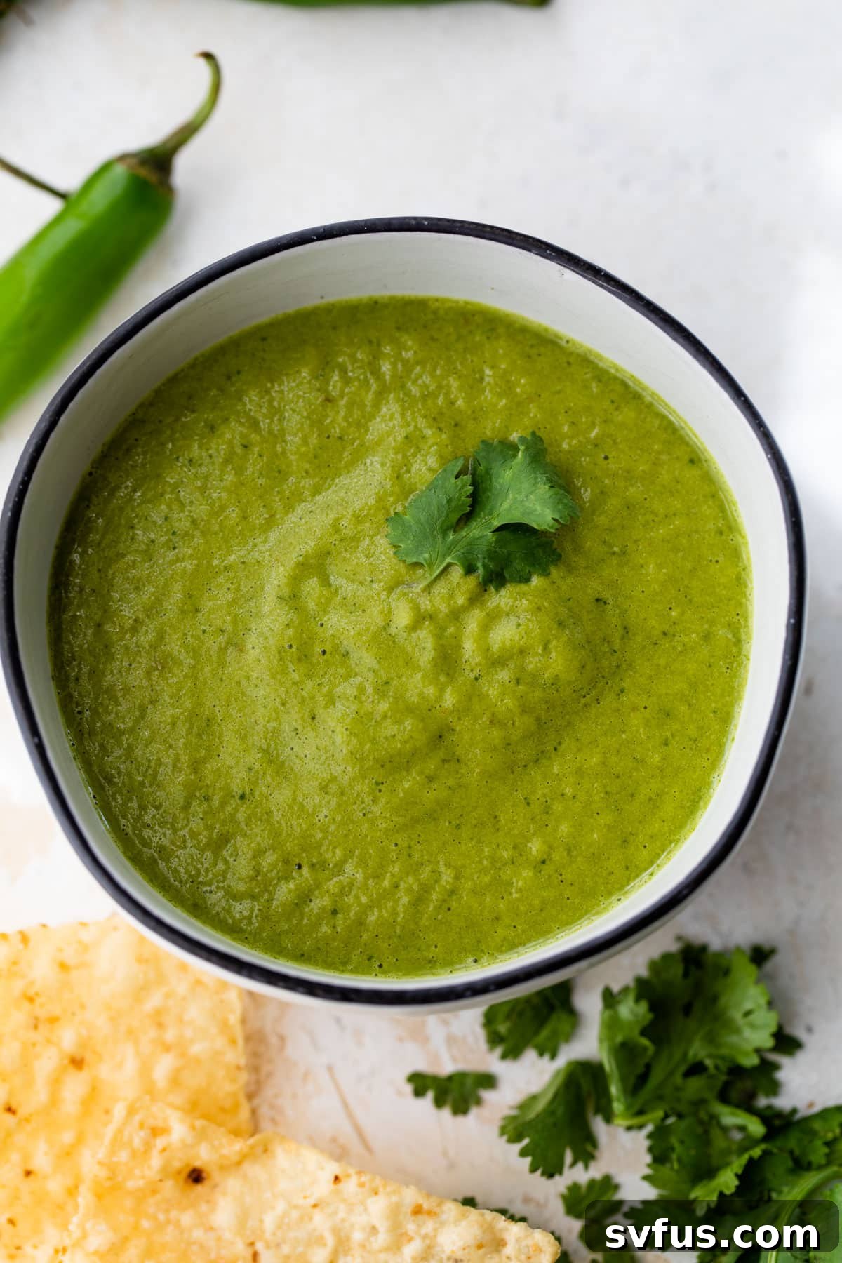 A beautiful bowl of bright green serrano salsa, generously garnished with fresh cilantro leaves on top.