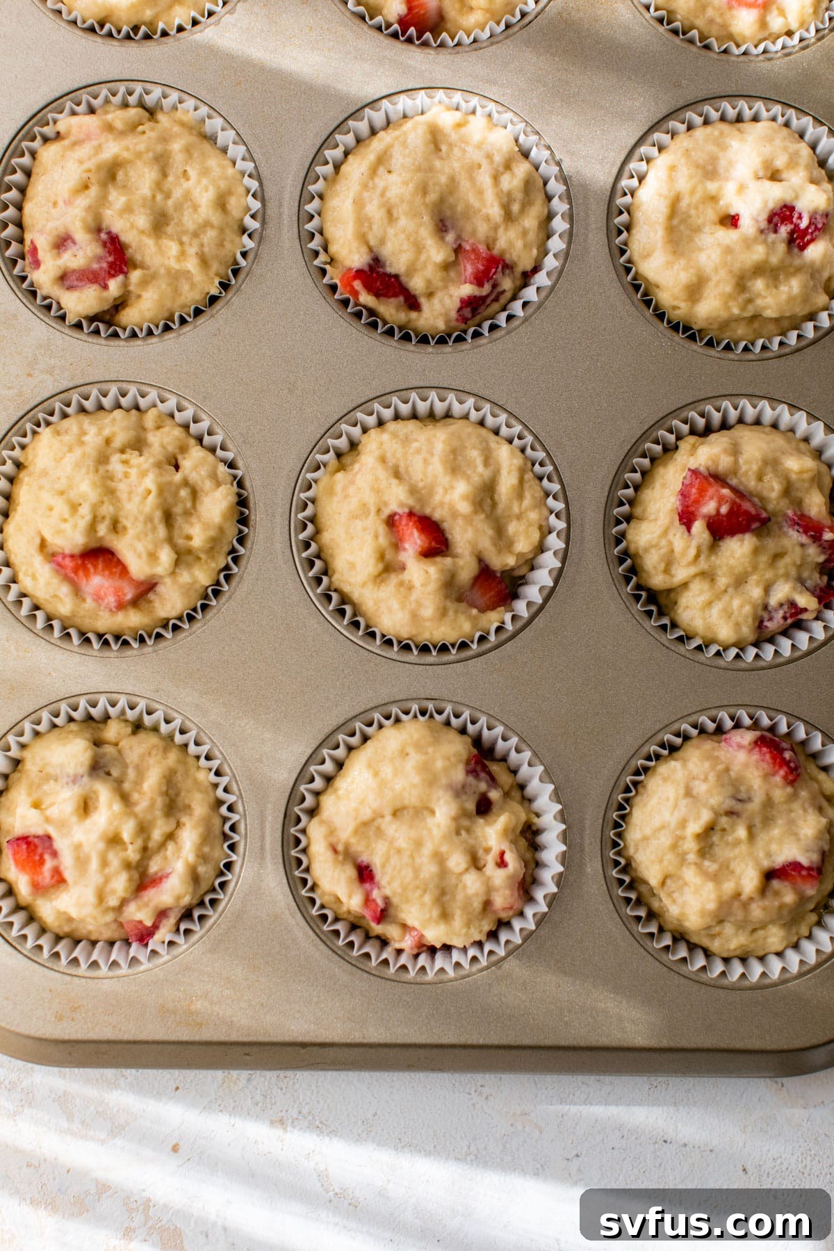 Muffin batter scooped into paper liners in a muffin tin, ready for baking.