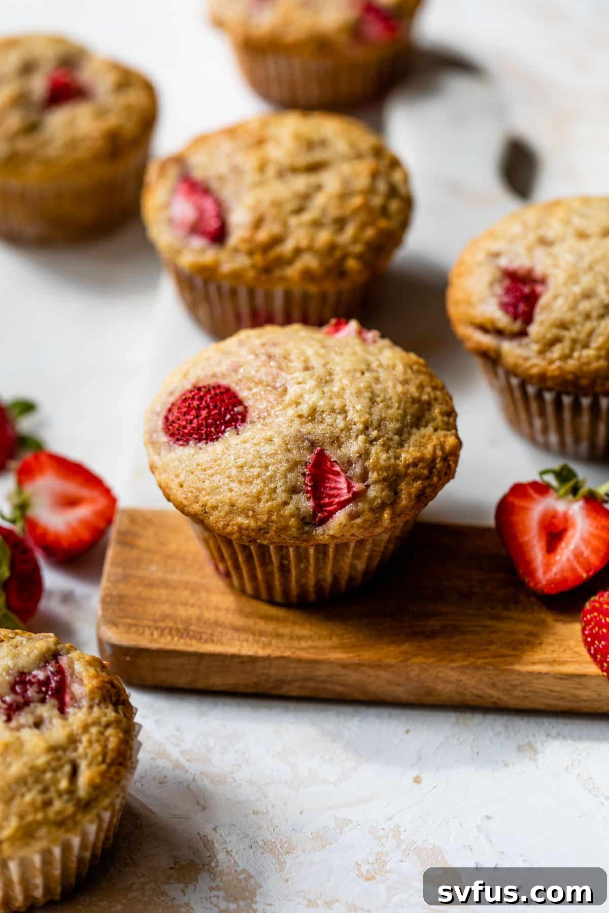 An overhead shot of freshly baked strawberry muffins cooling on a wire rack, with some on a cutting board.