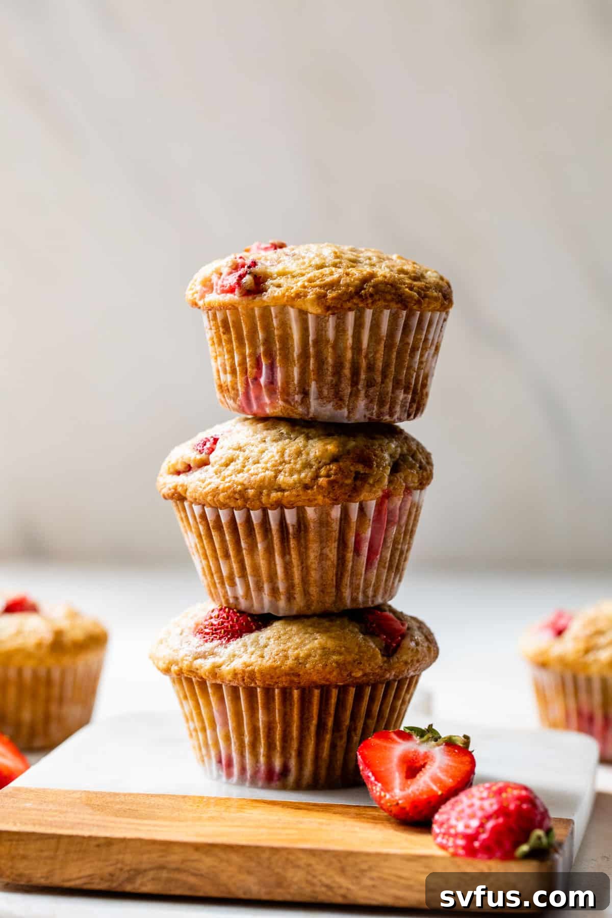 Side view of three fluffy strawberry muffins stacked on top of each other on a wooden cutting board.