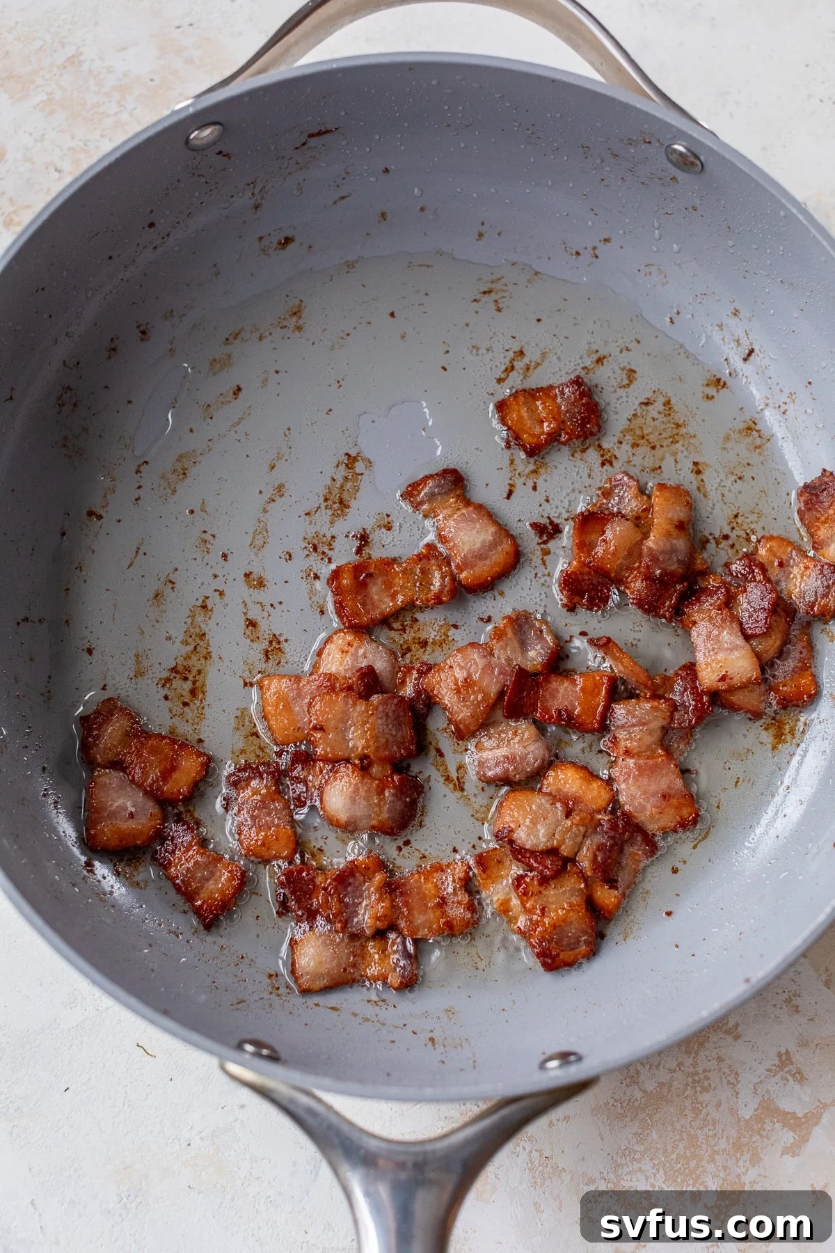 Chopped bacon cooking in a large skillet, sizzling to a perfect crisp.