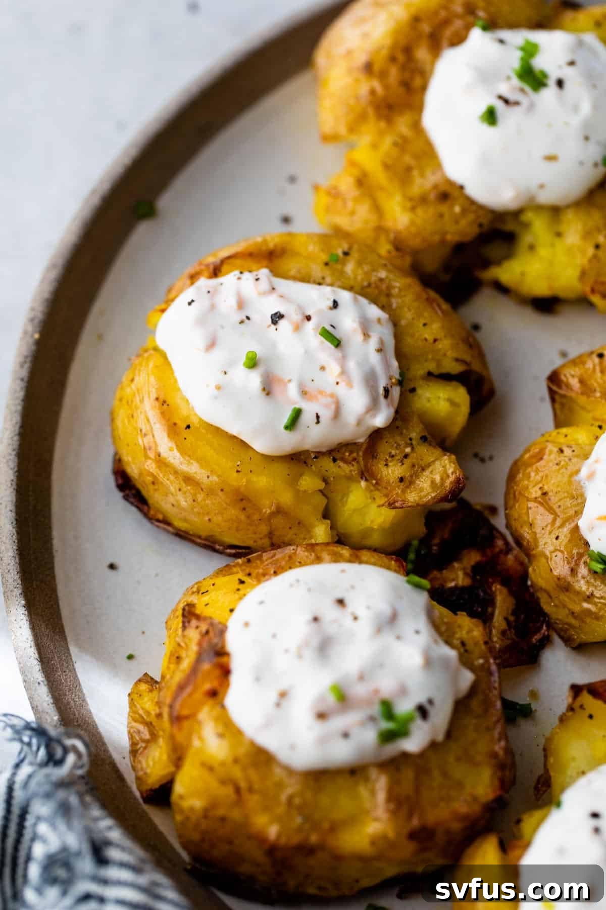 Close-up of crispy smashed potatoes on a plate with dollops of garlic cheddar sour cream on top, garnished with fresh chives