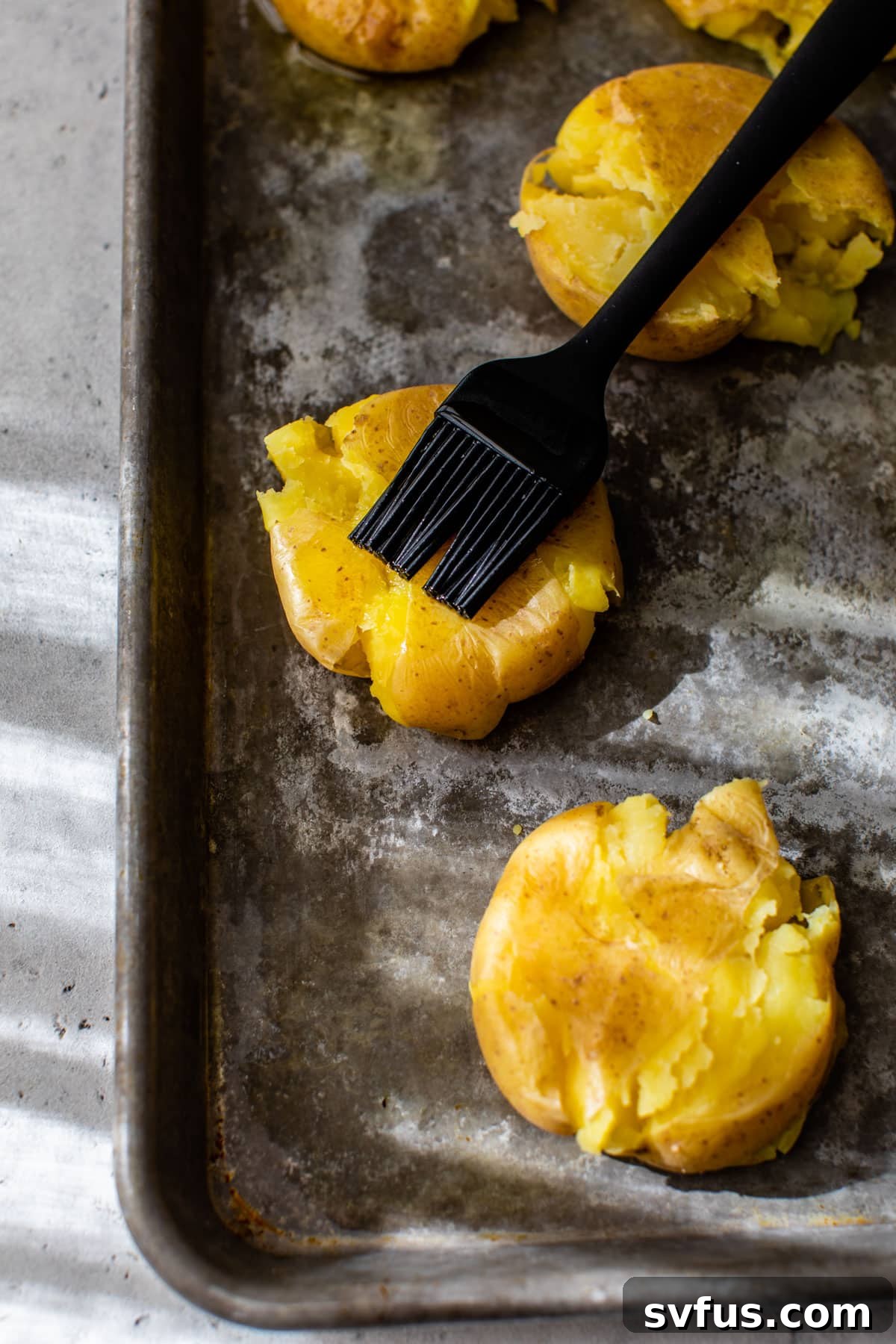 Smashed potatoes brushed with olive oil and seasoned on a baking sheet, ready for roasting
