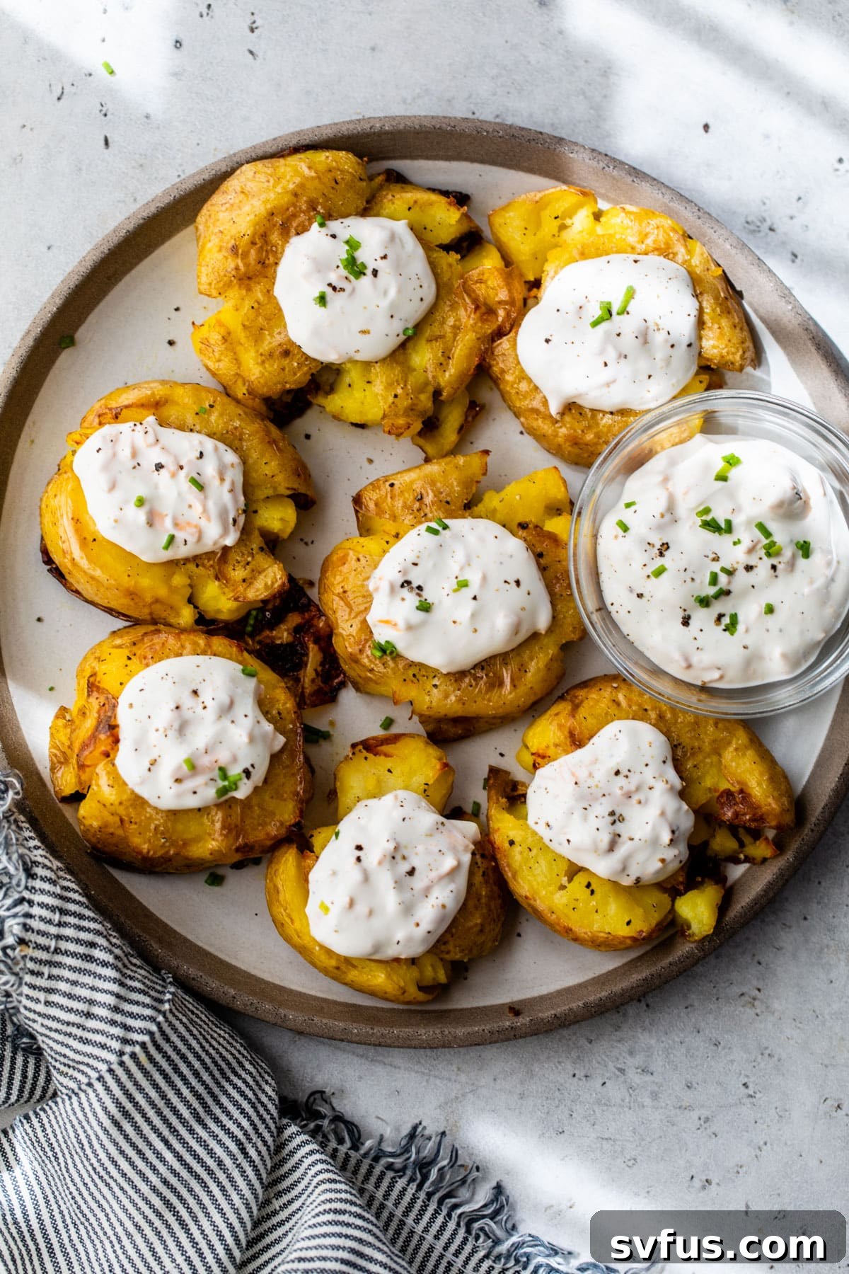 Crispy smashed potatoes arranged on a plate with dollops of garlic cheddar sour cream and fresh chives