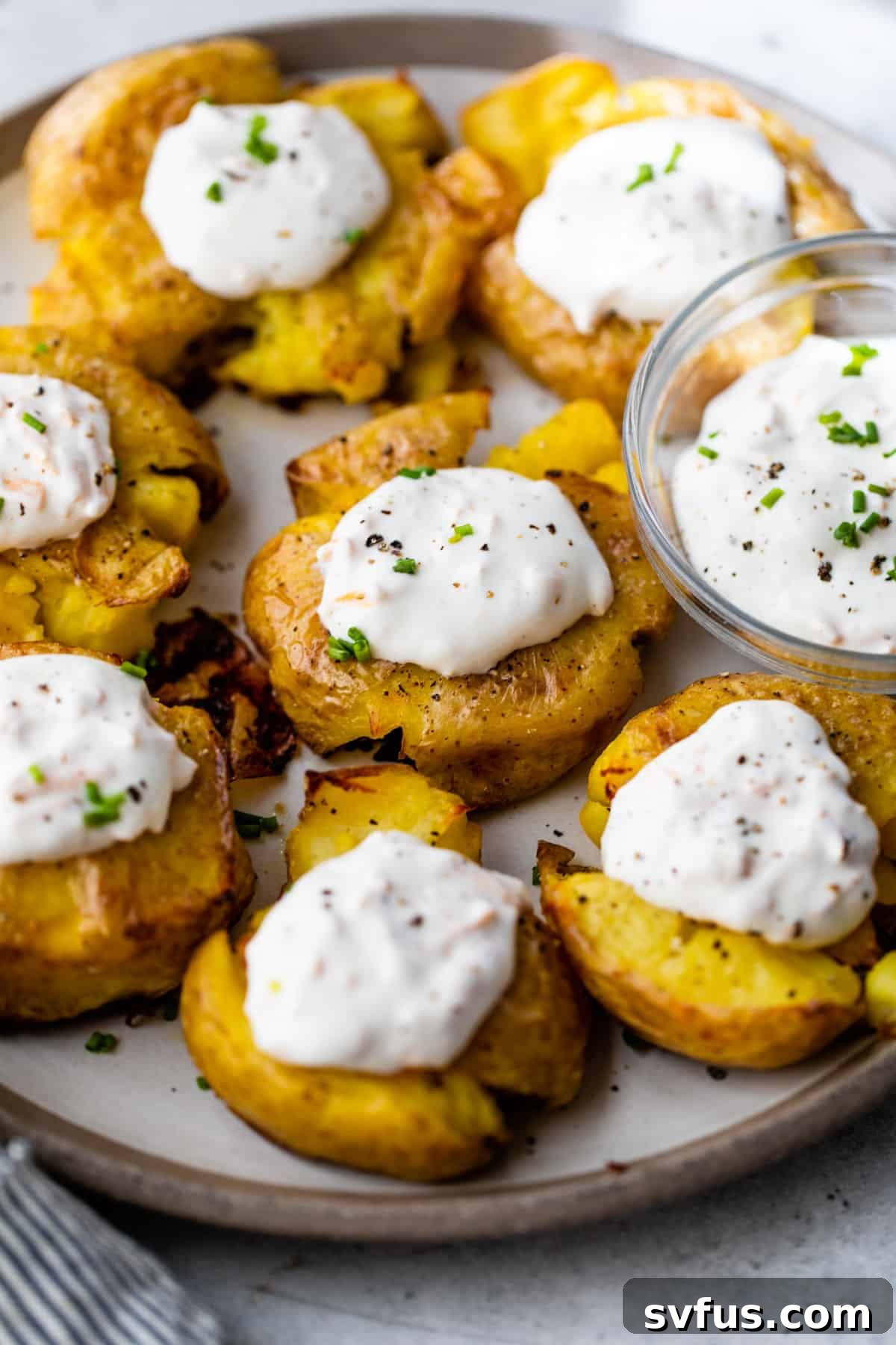 Overview of crispy smashed potatoes on a serving platter with dollops of garlic cheddar sour cream, ready to be enjoyed by all