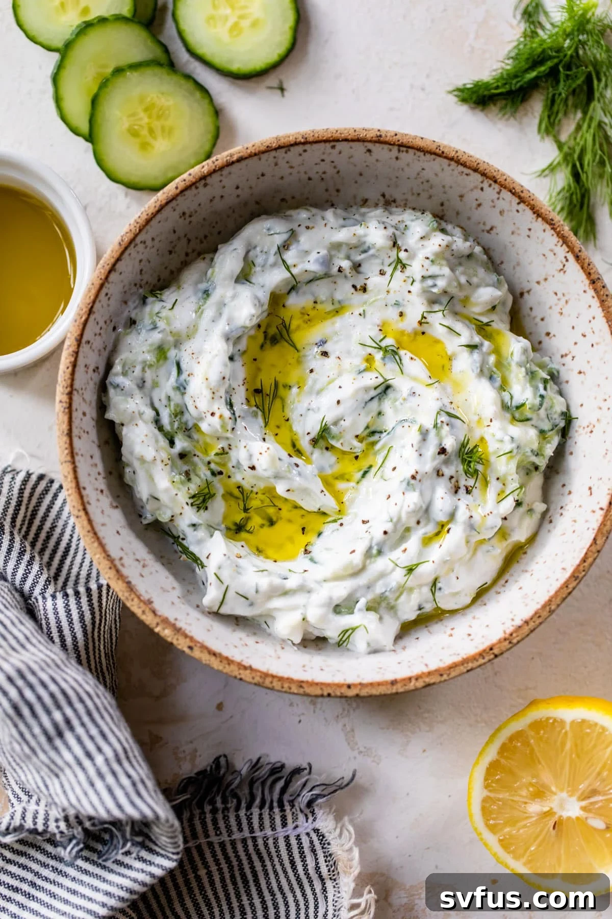 An inviting overhead view of homemade tzatziki sauce in a serving bowl, beautifully garnished with a swirling drizzle of olive oil on its surface.