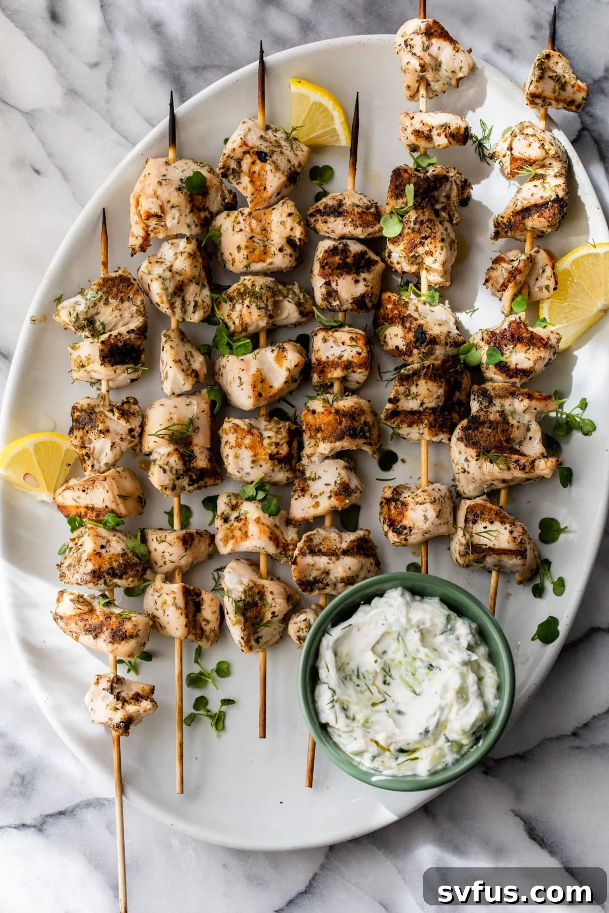 Close-up of golden brown Greek chicken skewers artfully arranged on a white plate, with a side of creamy tzatziki sauce and fresh herbs, ready to be served.