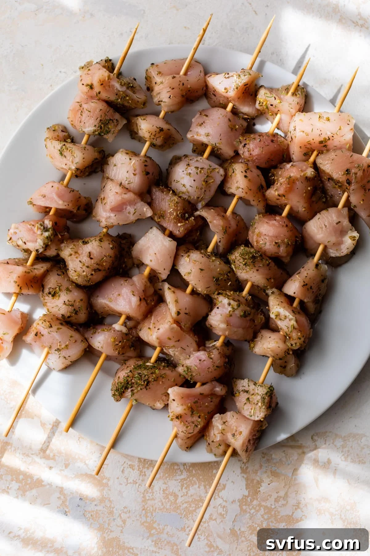 Marinated chicken pieces expertly threaded onto wooden skewers, resting on a white plate, ready for grilling.