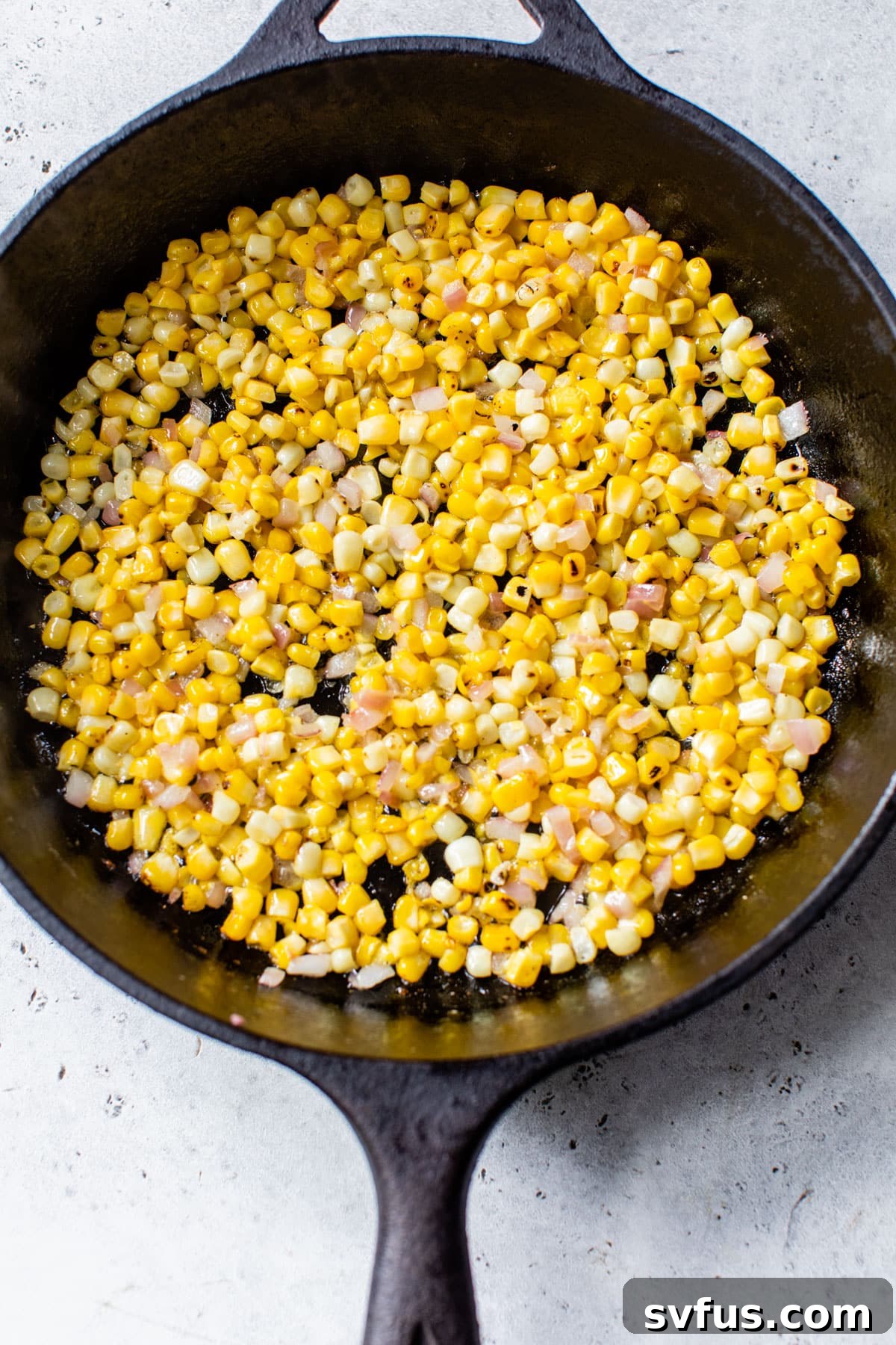 Diced red onions and fresh corn kernels beginning to sauté in a cast iron skillet with melted butter.