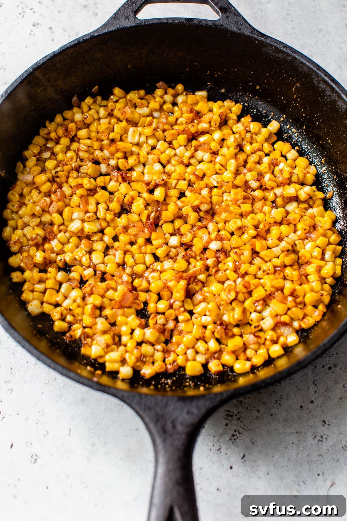 Close-up of corn and onions simmering in a cast iron skillet, coated in a smoky seasoning blend.