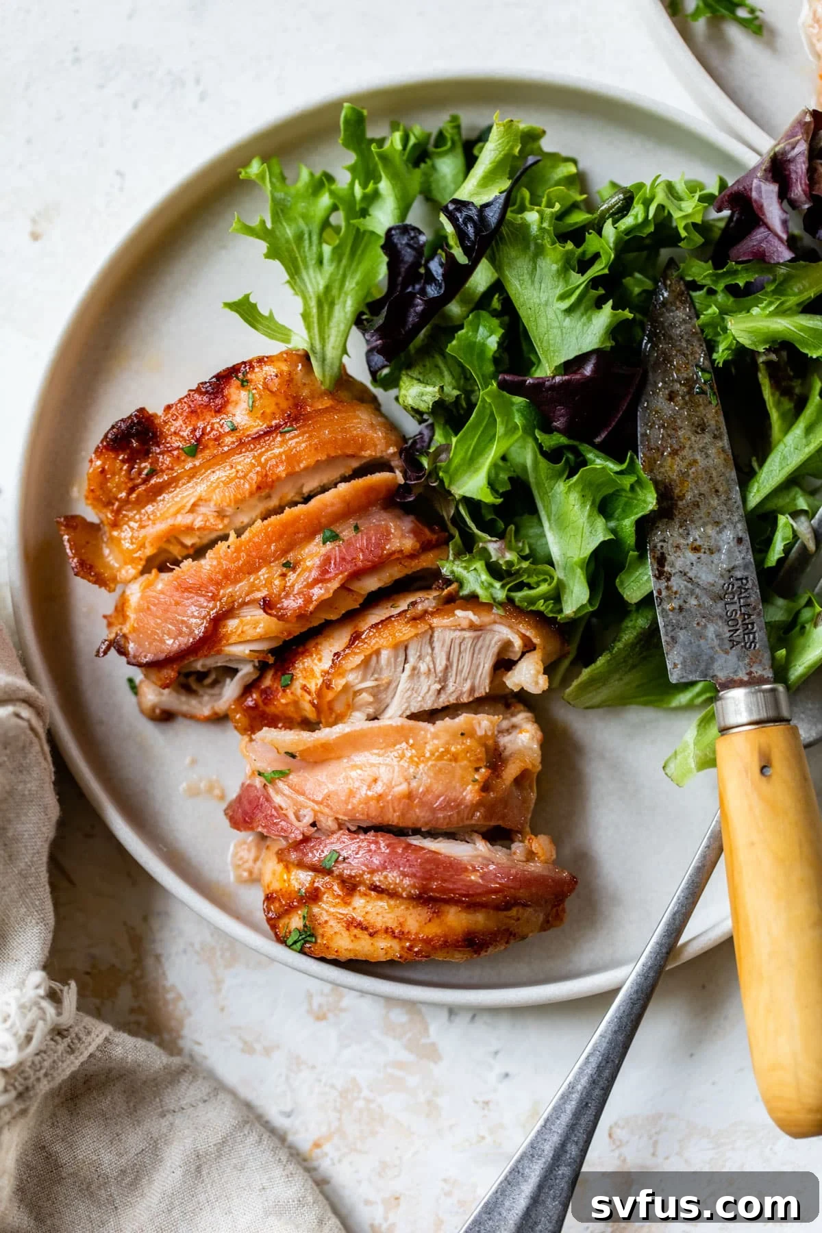 sliced bacon-wrapped chicken thigh on a plate with lettuce and a knife, showcasing crispy bacon and juicy chicken