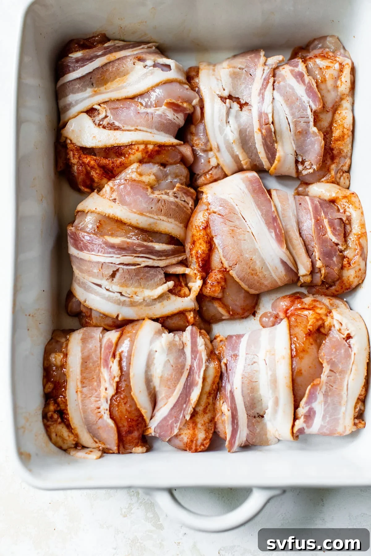 bacon wrapped around chicken thighs arranged in a baking dish before cooking