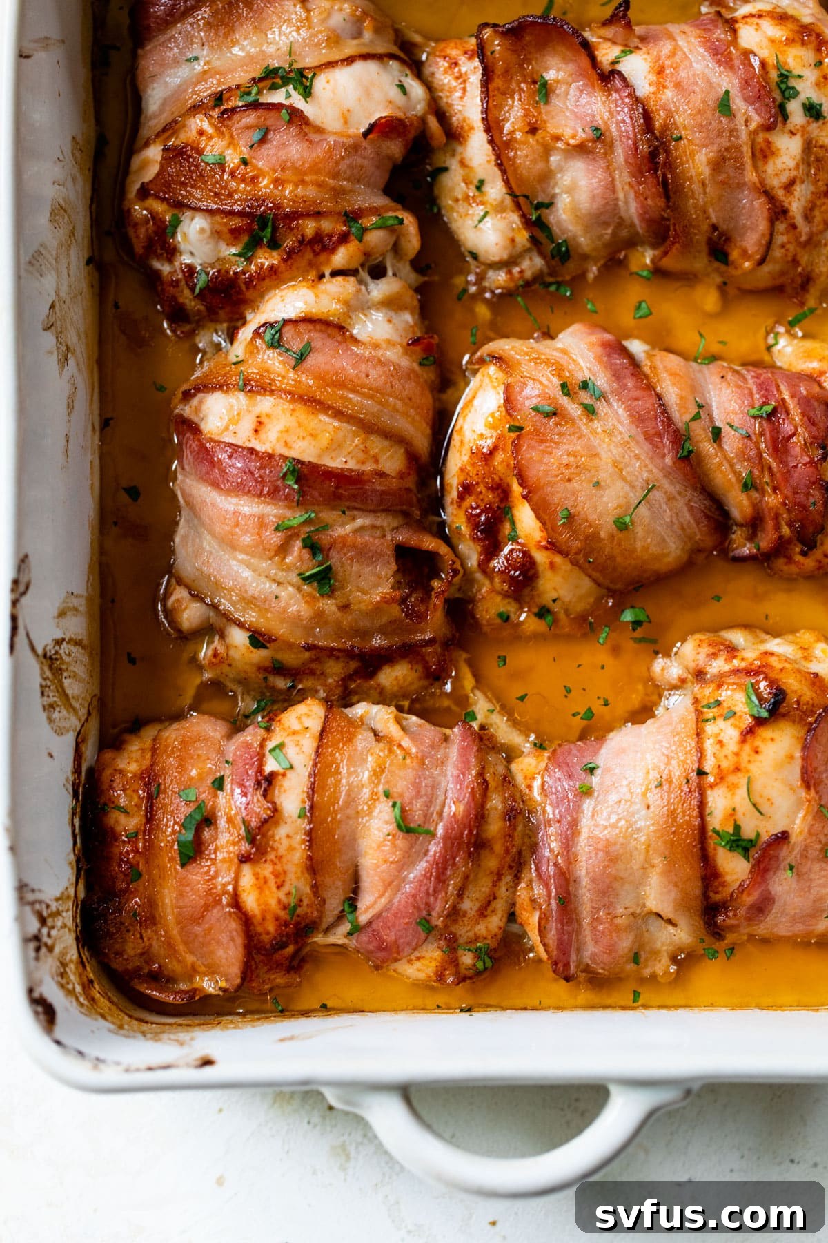 cooked bacon wrapped around chicken thighs presented in a baking dish, ready to be served